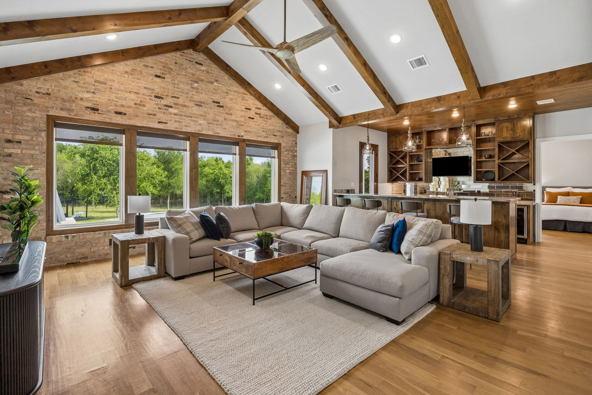 Living room with vaulted timber-beam ceiling, brick wall, large sectional, and built-in shelving.