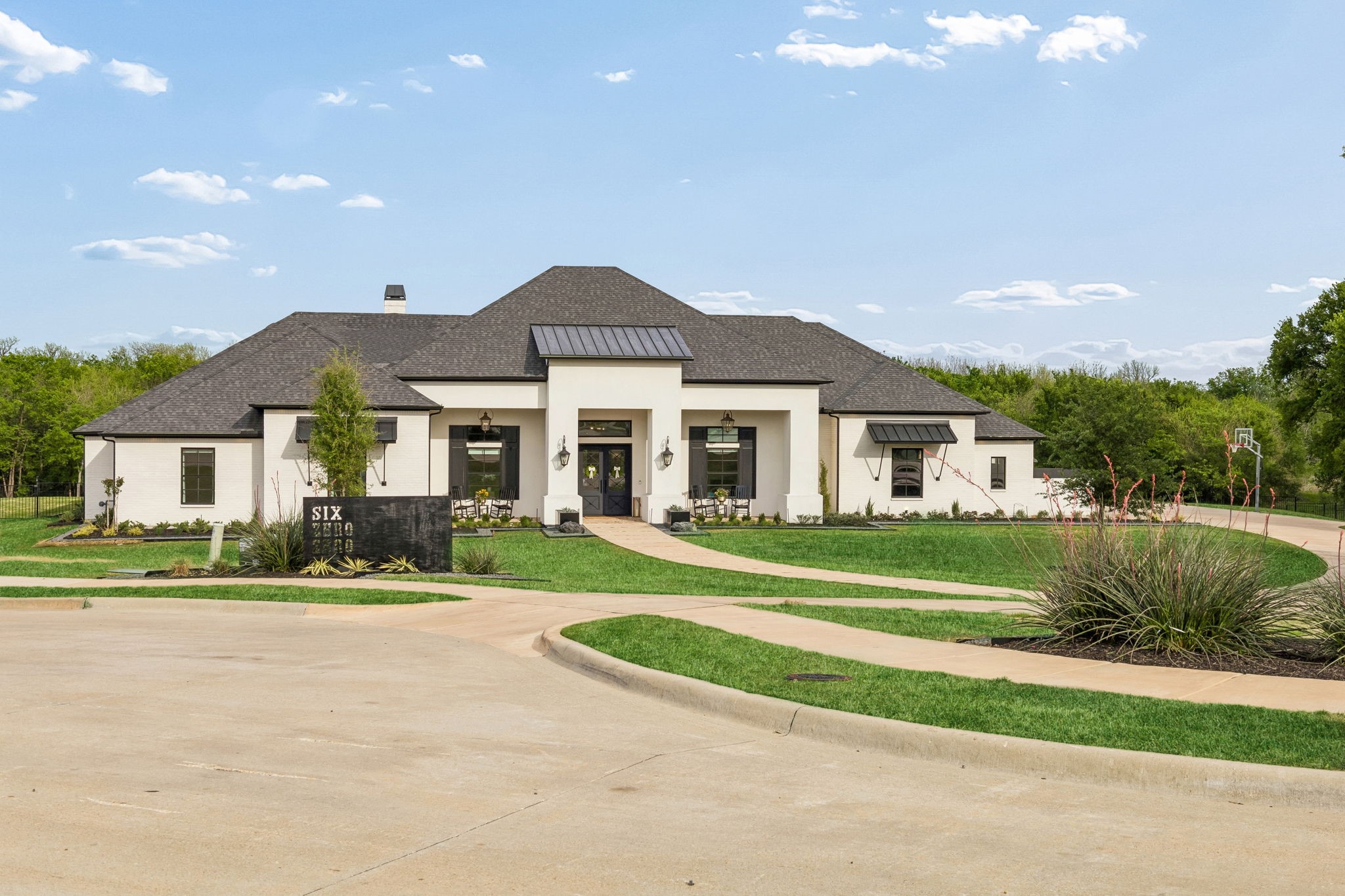 White-brick home with a dark hipped roof, landscaped lawn, and curved front walkway.