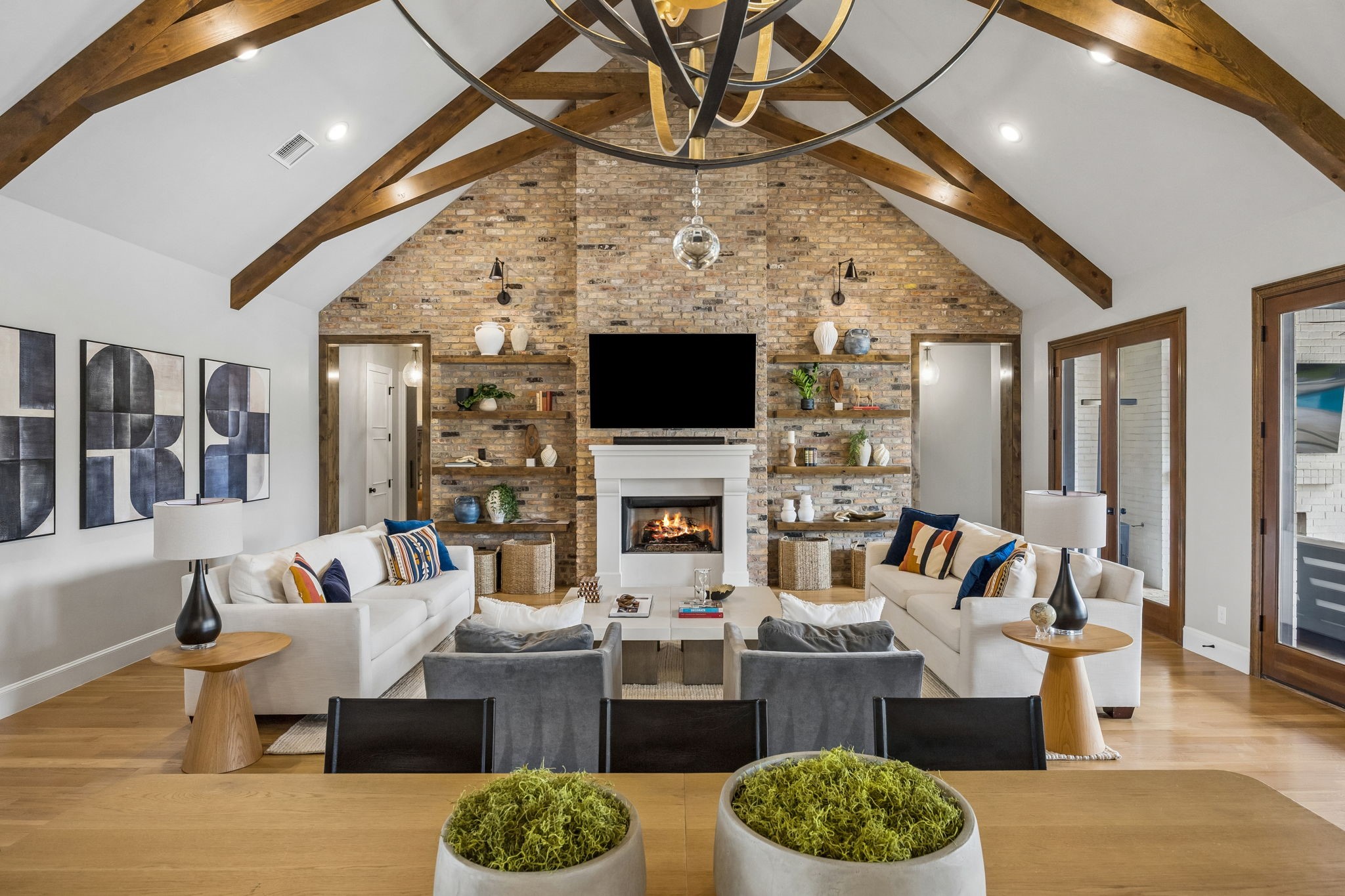 Vaulted living room with exposed wood beams, brick fireplace, built-in shelves, and white sofas.