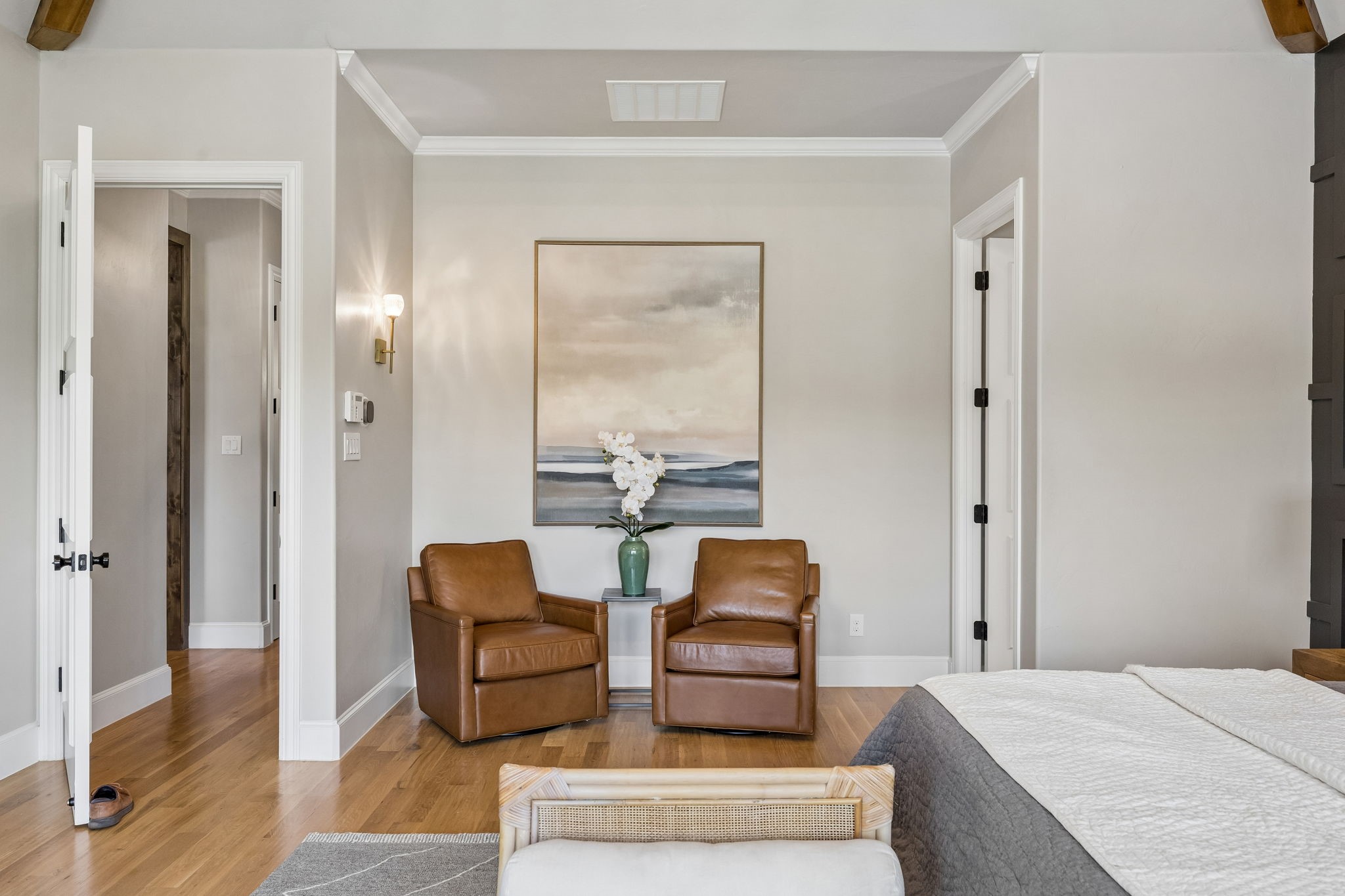 Bedroom with two brown leather armchairs and white orchids beneath framed artwork.