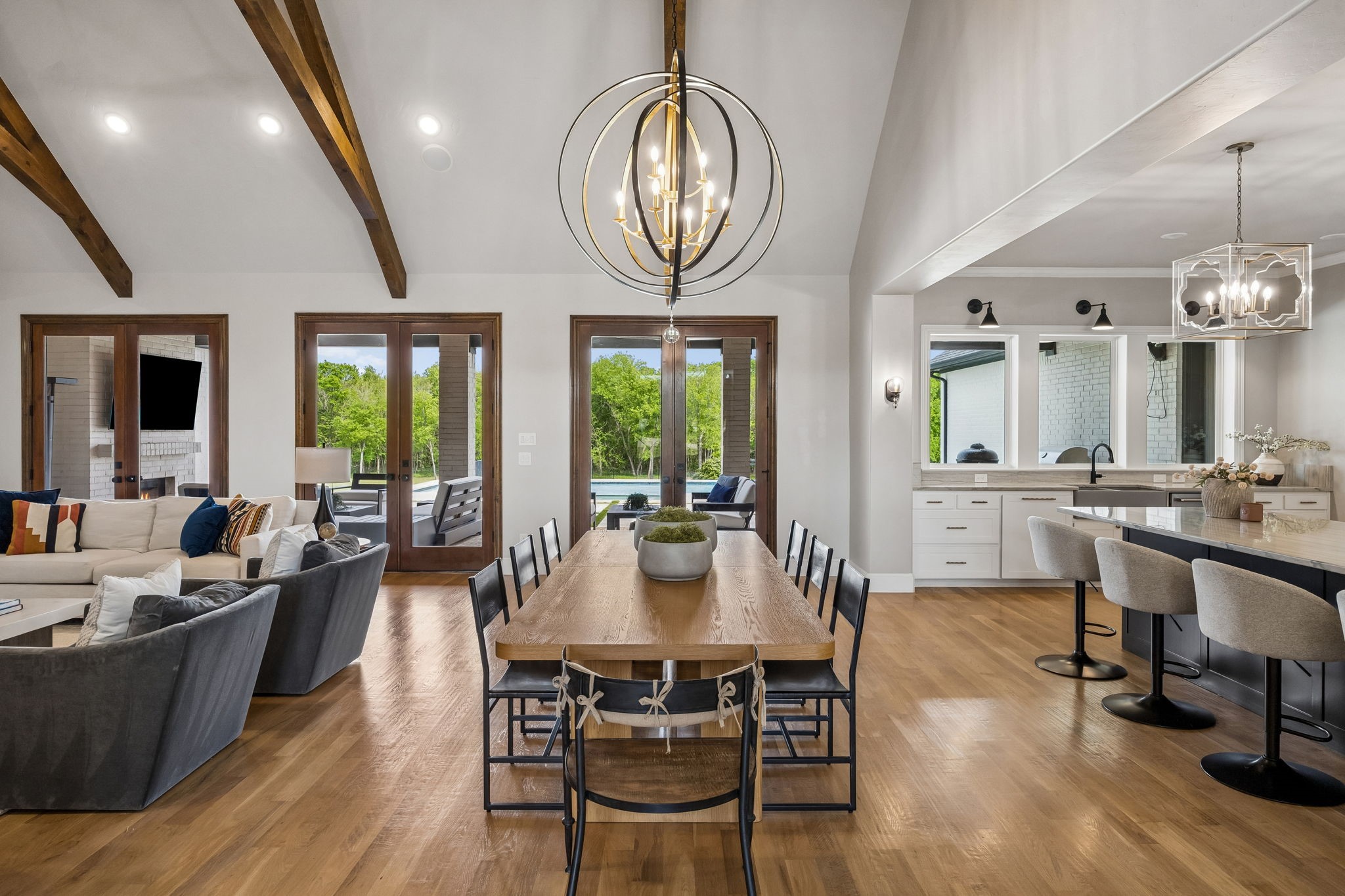 Open-plan dining area with exposed wood beams, a long table, and glass doors overlooking the pool.