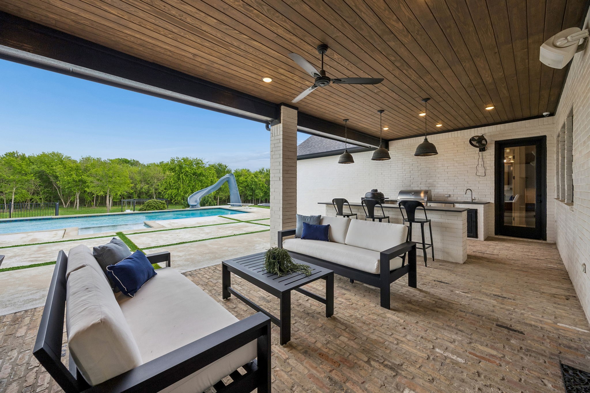 Covered patio with cushioned seating and an outdoor bar overlooking a pool with a slide.