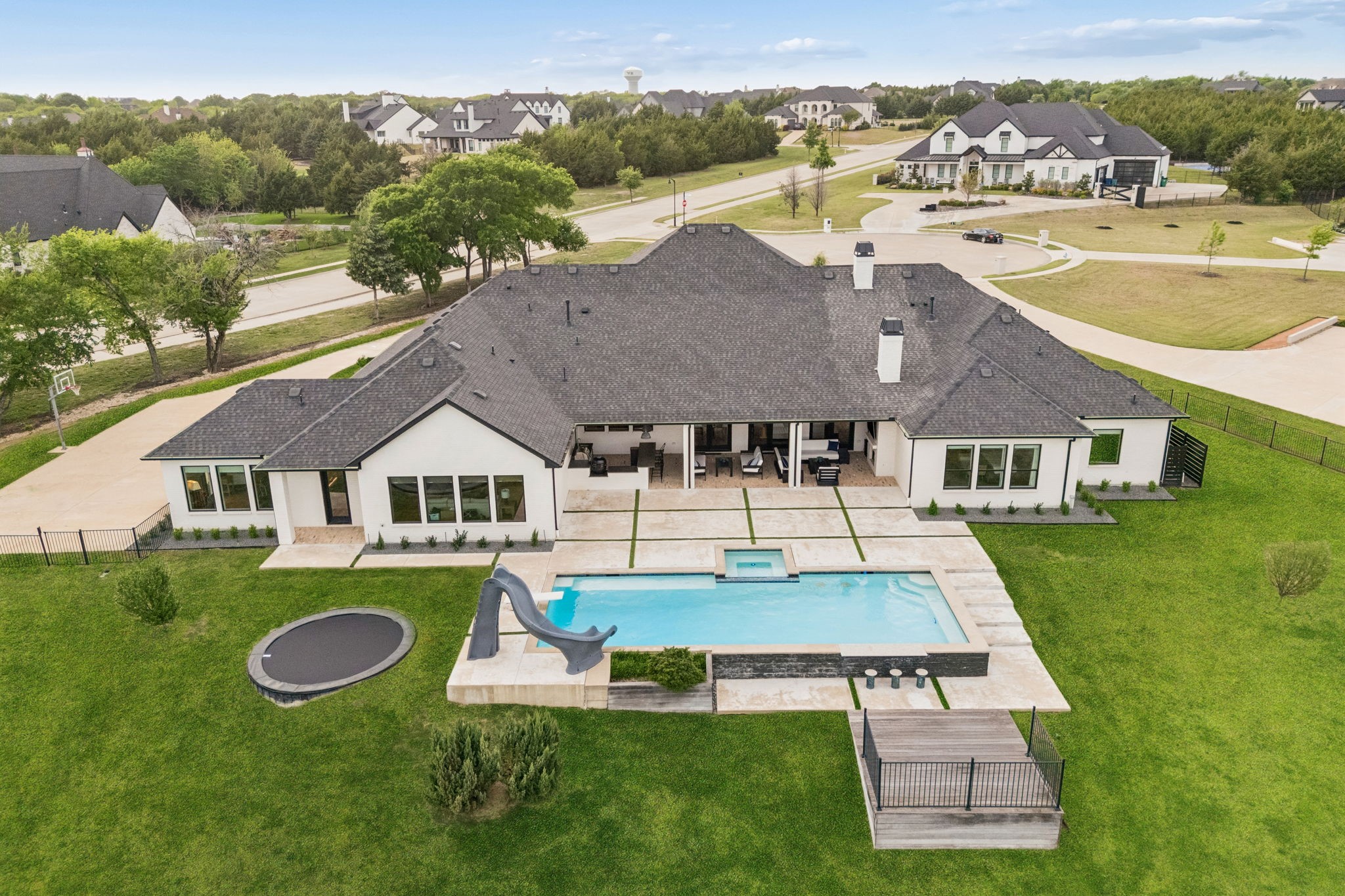 Aerial view of a white home with a pool, spa, slide, and trampoline in the backyard.