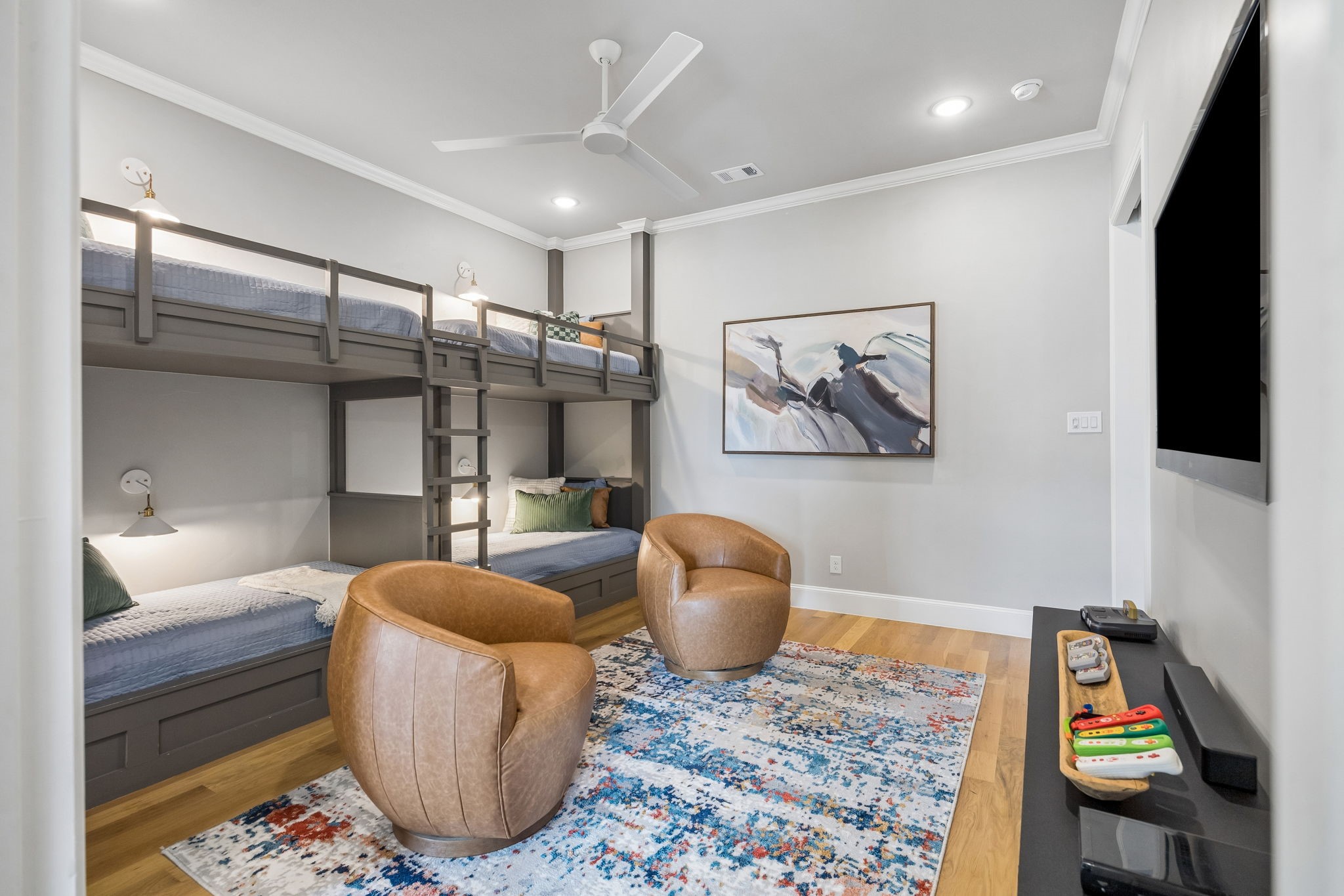 Bedroom with built-in gray bunk beds, tan leather chairs, and a colorful patterned rug.