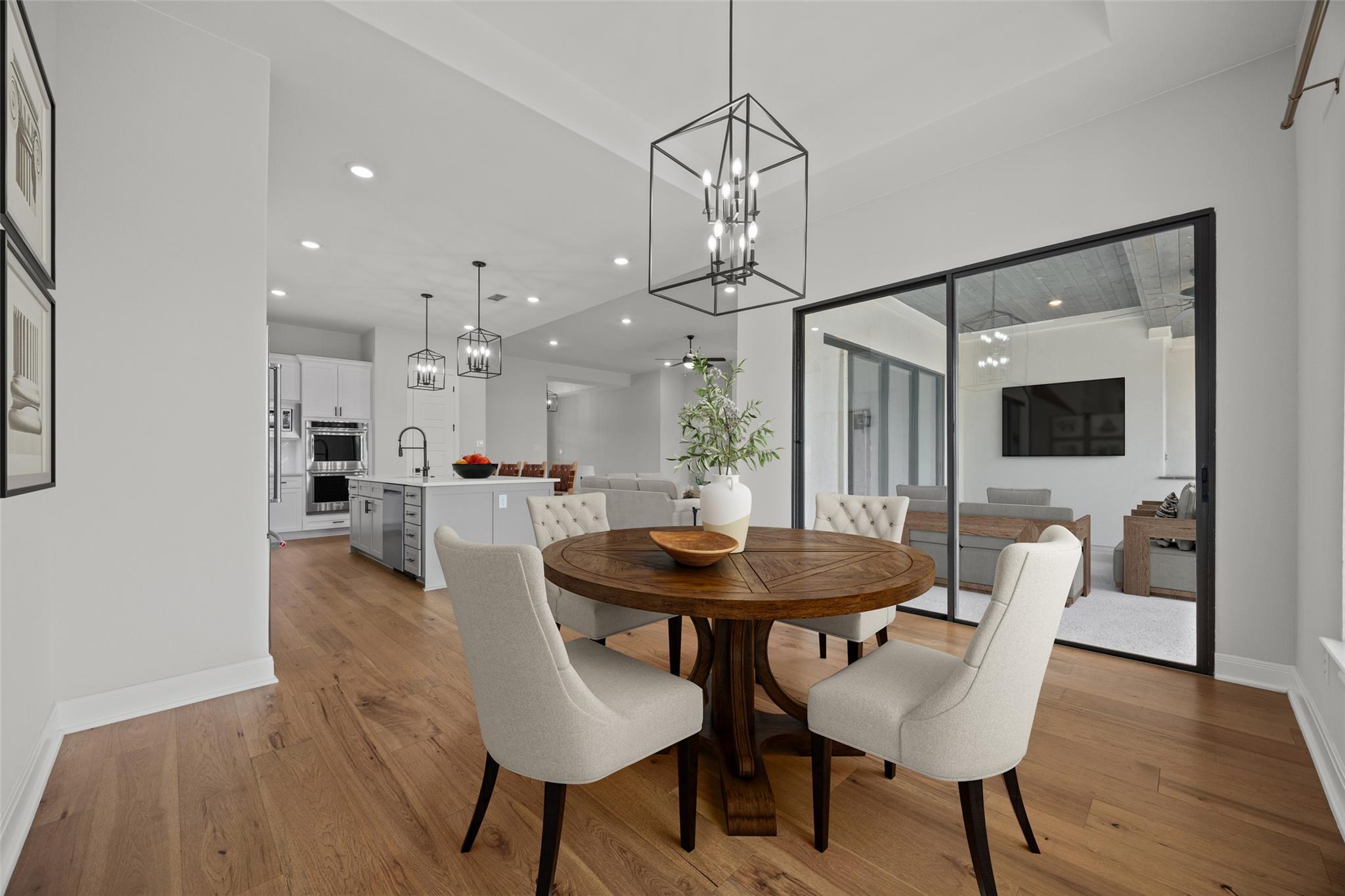 Dining area with a round wooden table, white chairs, hardwood floors, and a view into the kitchen and living room.