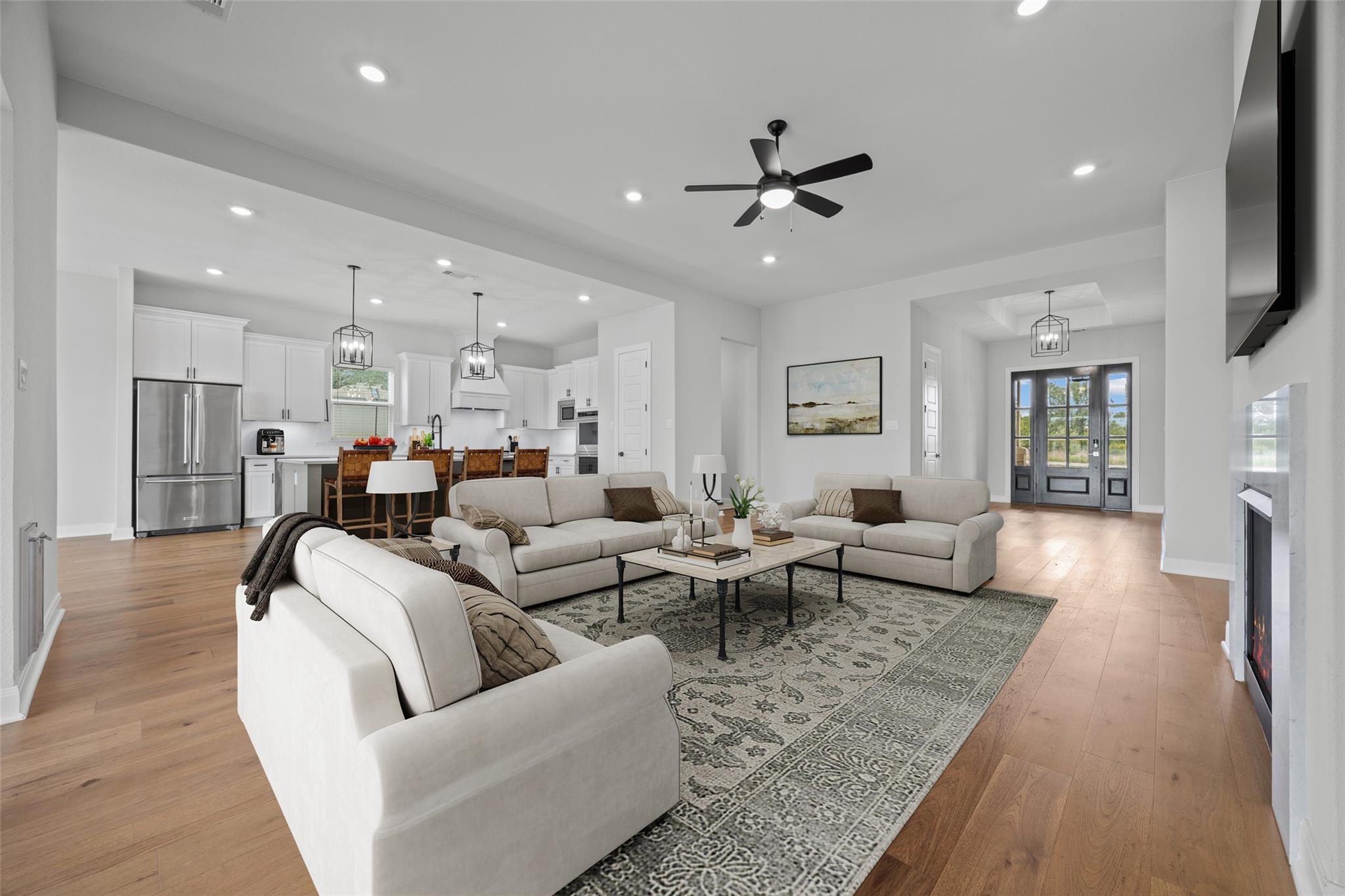 Open-plan living room and kitchen with neutral sofas, white cabinetry, and black-framed glass doors.