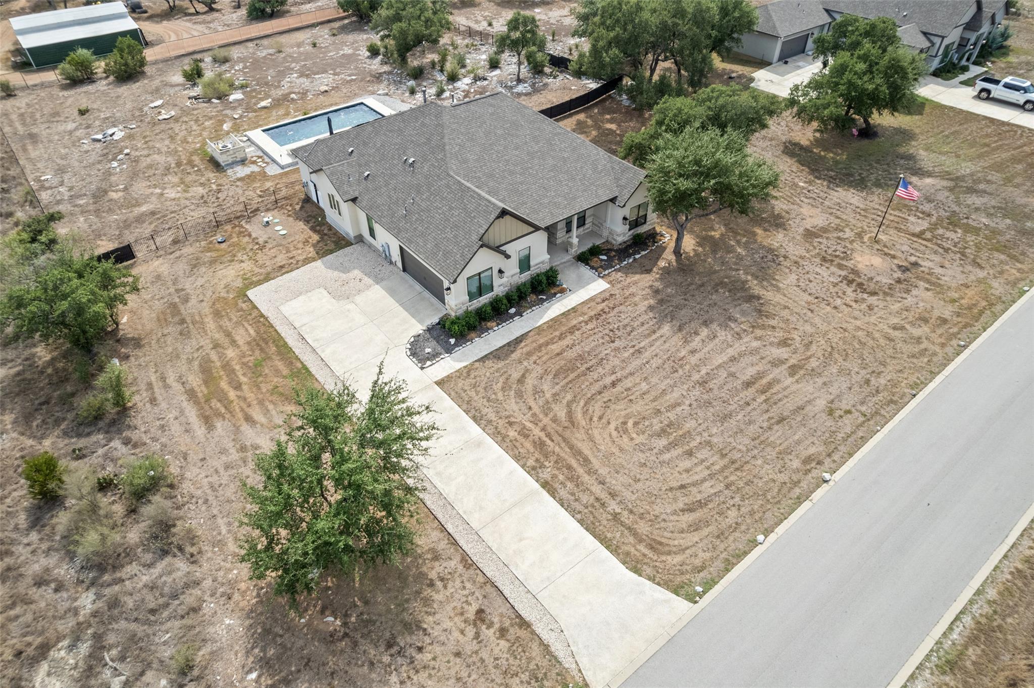 Aerial view of a single-story home with a long driveway, dry yard, and backyard pool.