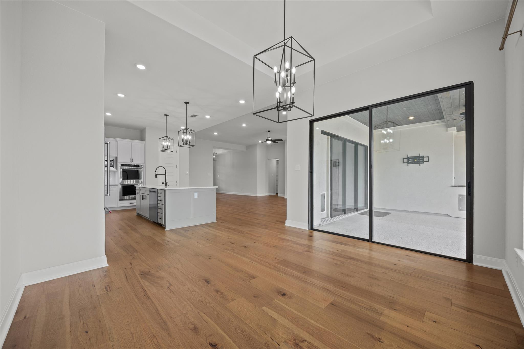 Open-plan kitchen and living area with wood floors, pendant lights, and sliding glass doors to a patio.