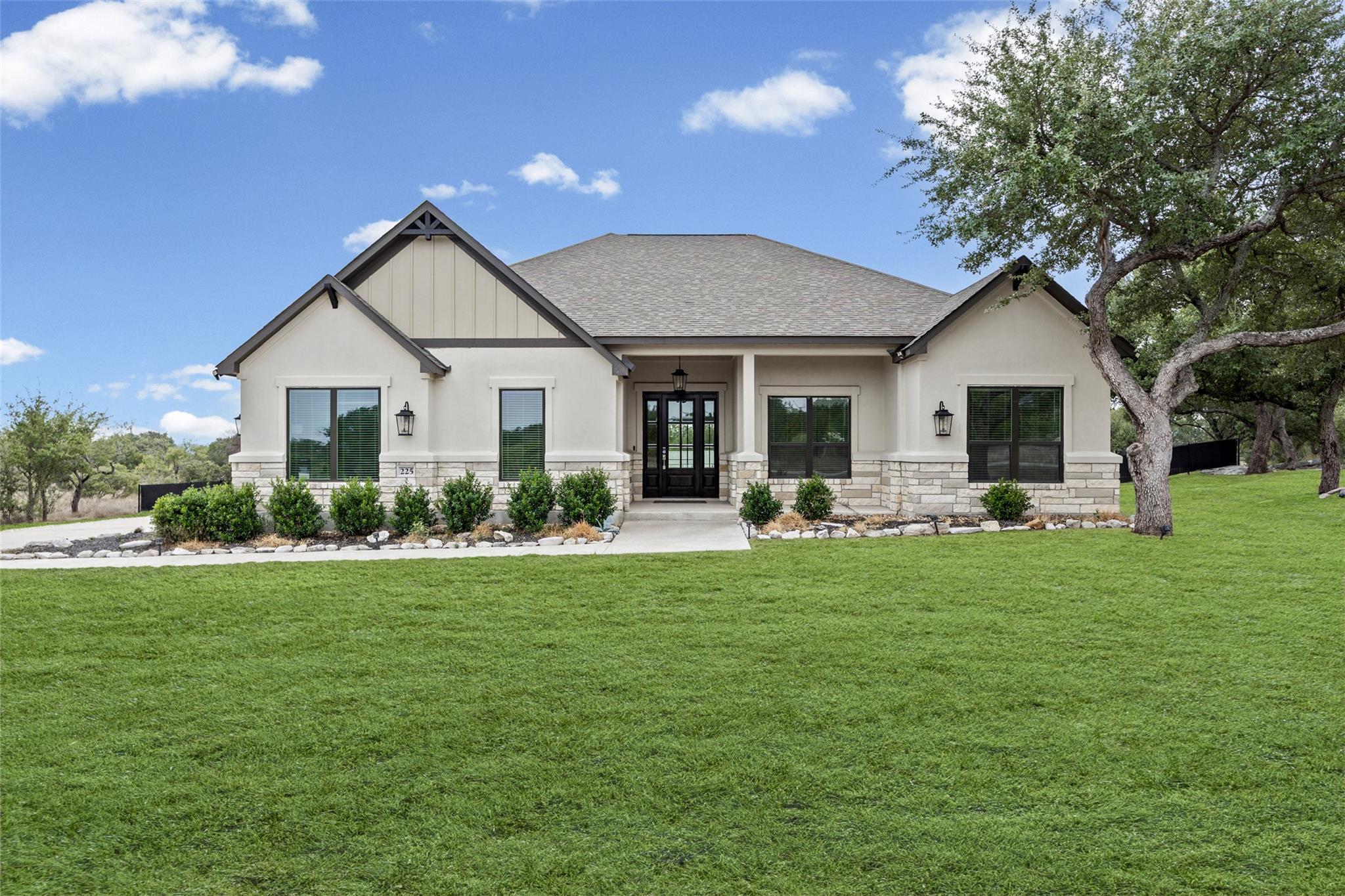 Home exterior with stone accents, a covered entry, broad lawn, and mature oak tree.