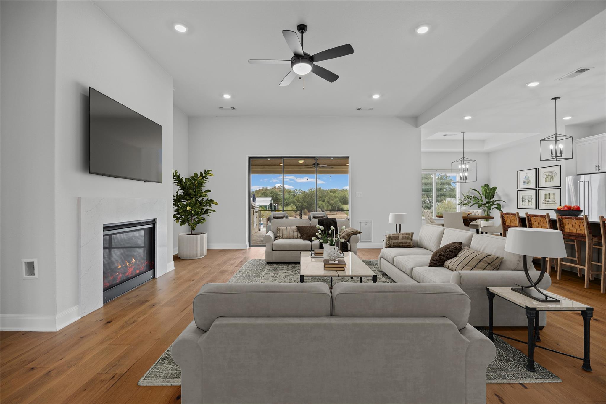 Open-plan living room with a fireplace, white sofas, hardwood floors, and sliding doors to a wooded view.