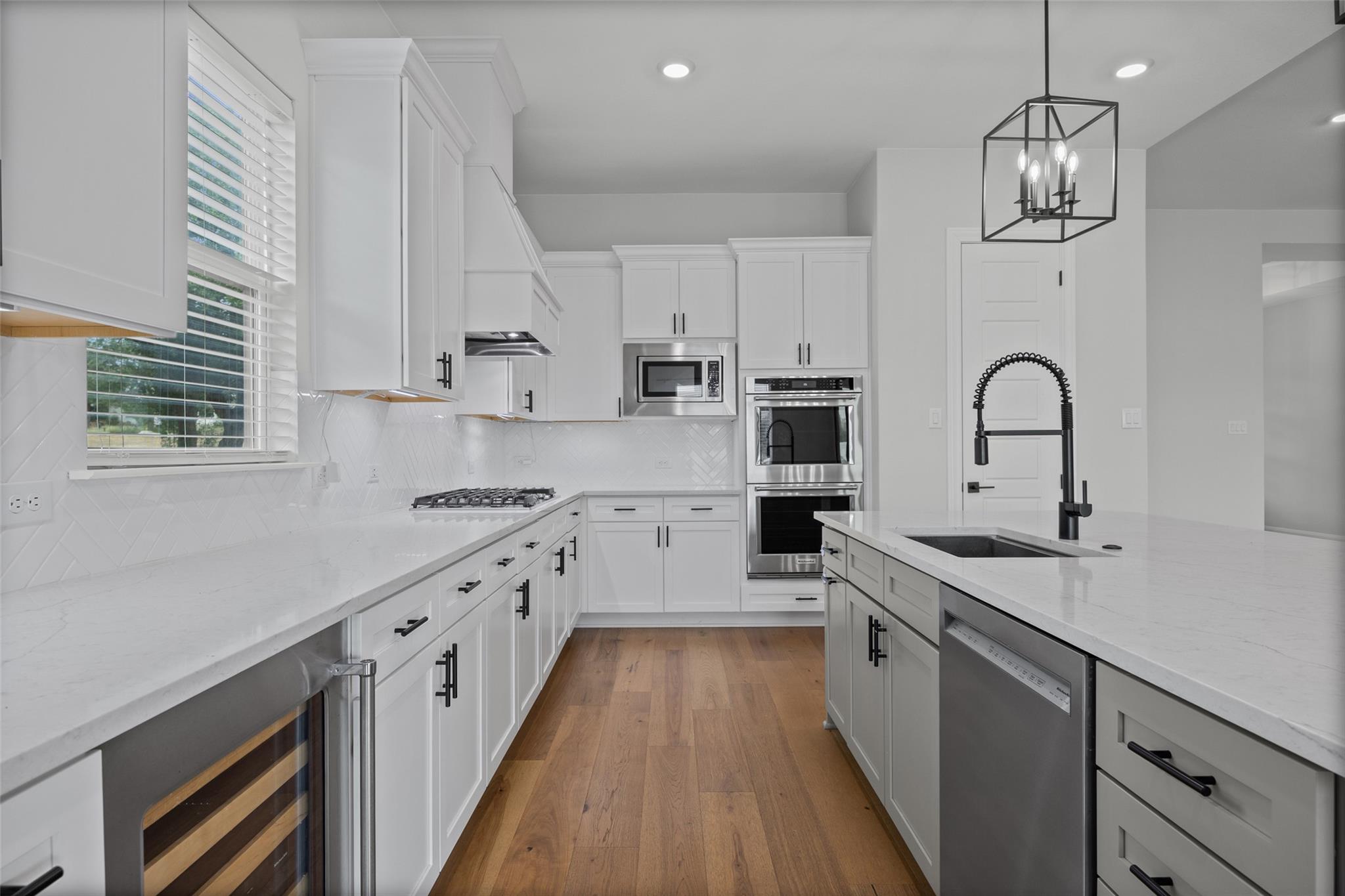 Modern white kitchen with a large island, stainless steel appliances, and warm wood floors.