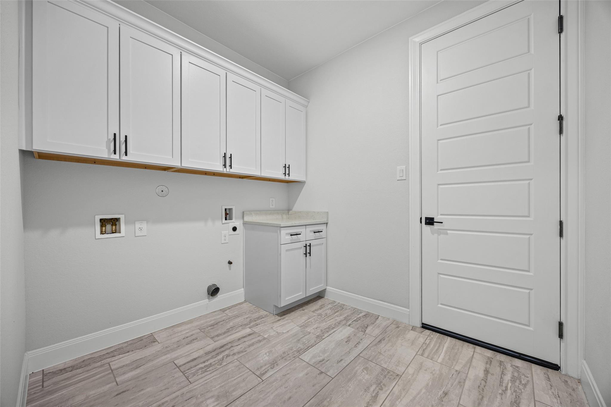 Laundry room with white cabinets, washer and dryer hookups, and gray wood-look tile flooring.