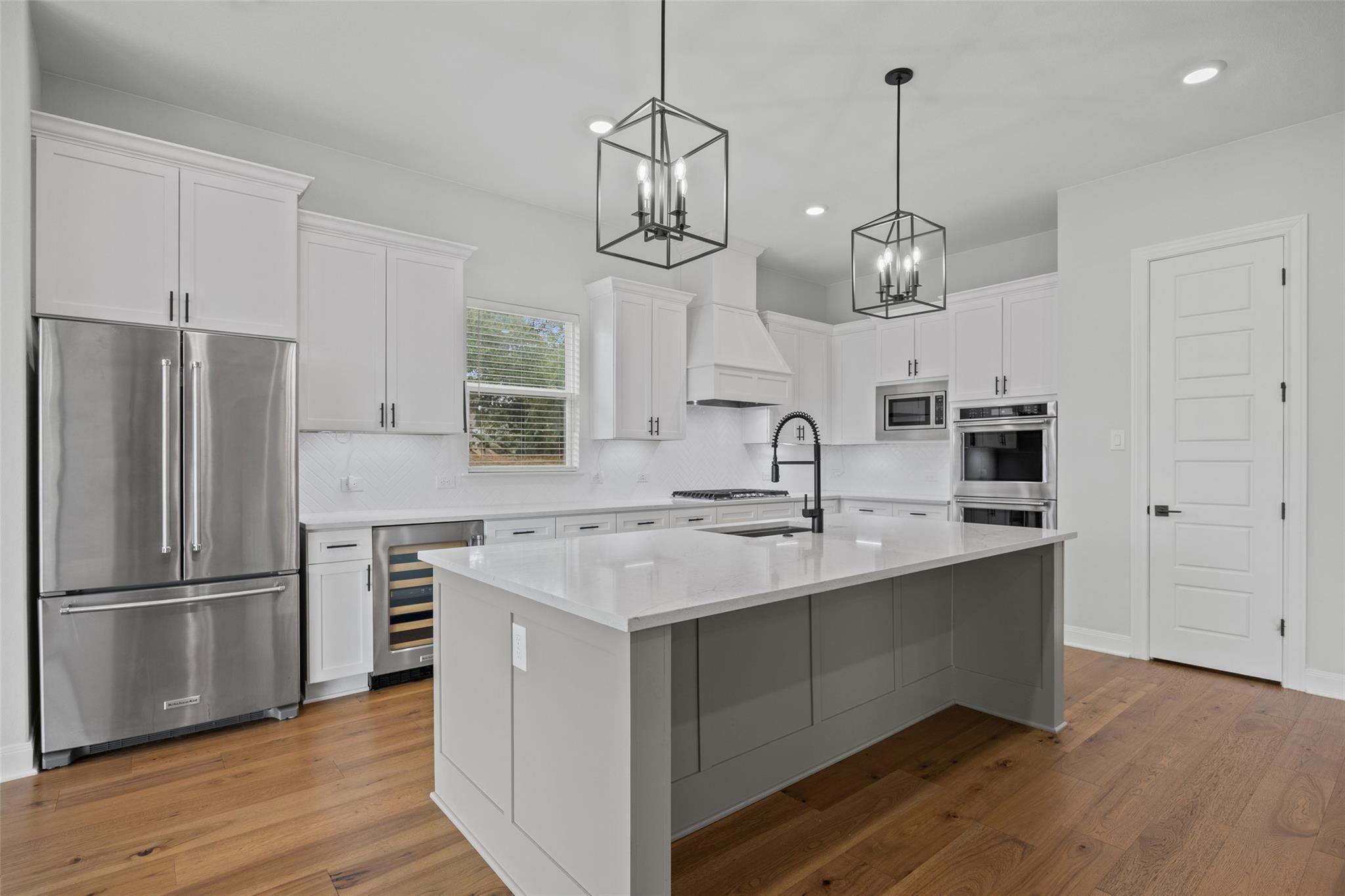 Modern kitchen with a large gray island, white cabinets, and stainless steel appliances.