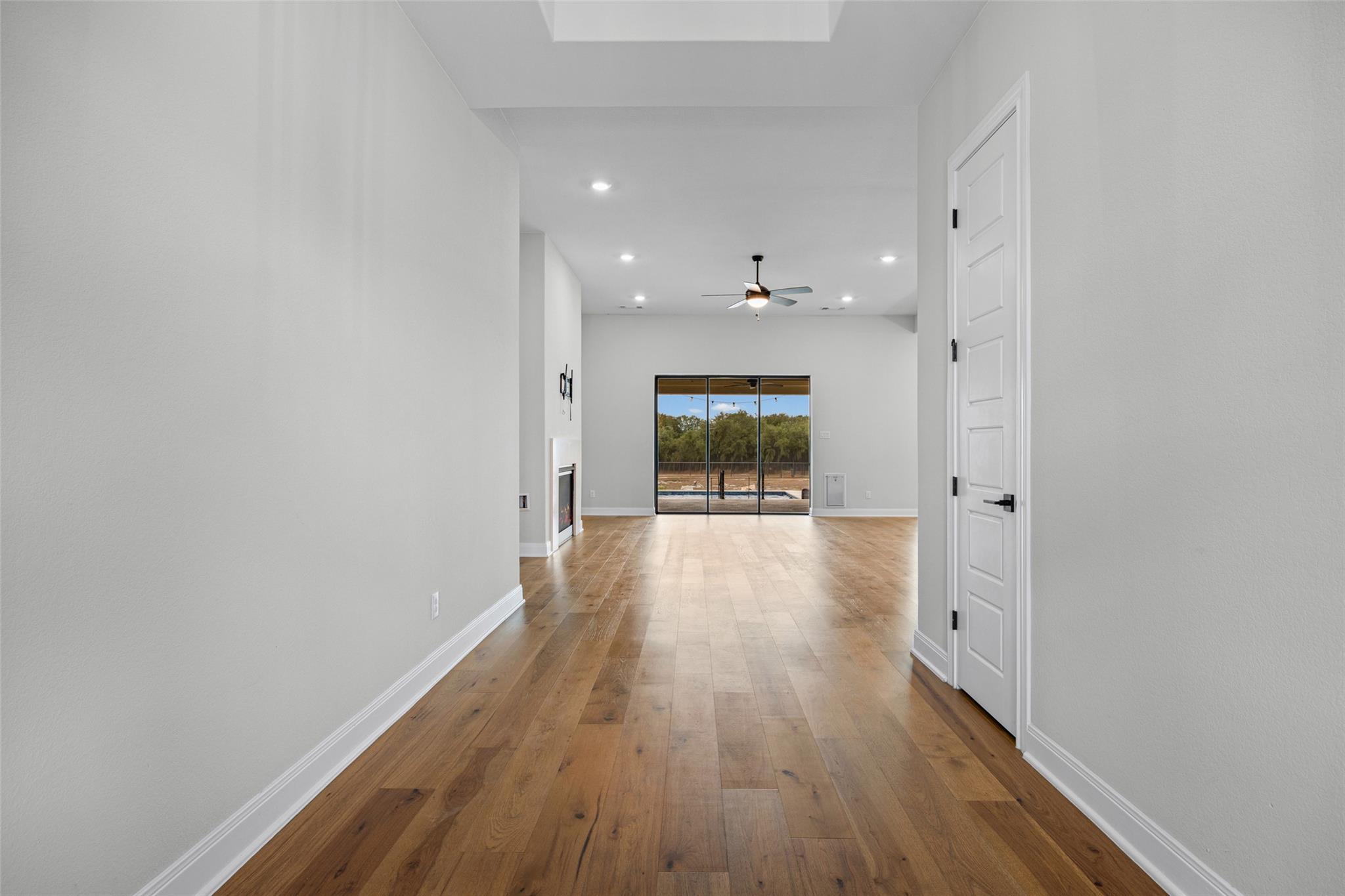 Open living area with wood floors, a fireplace, and sliding glass doors overlooking a pool and trees.