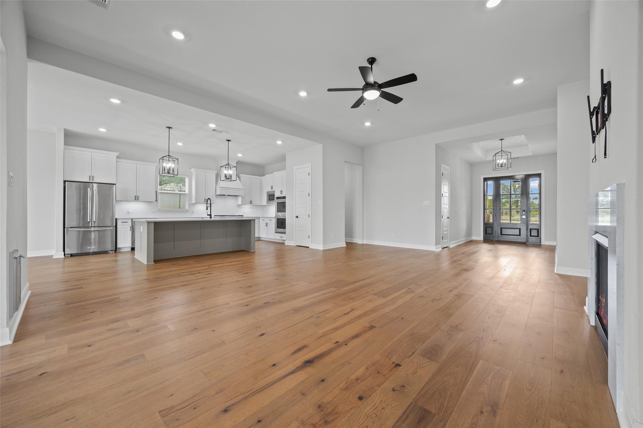 Open-plan kitchen and living area with a gray island, hardwood floors, and black-framed glass entry doors.
