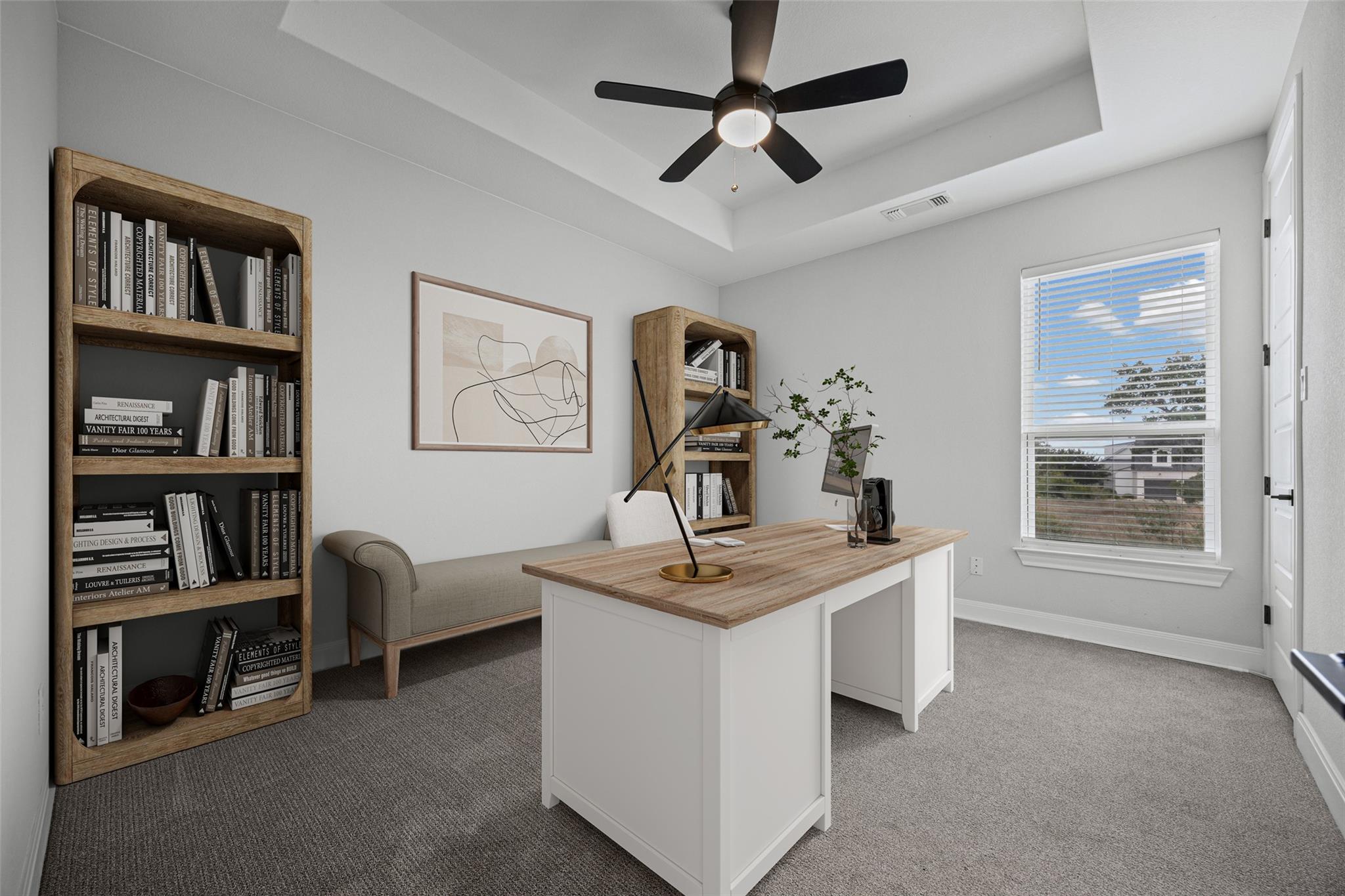 Furnished home office with a wood-topped desk, bookcases, small sofa, and black ceiling fan.