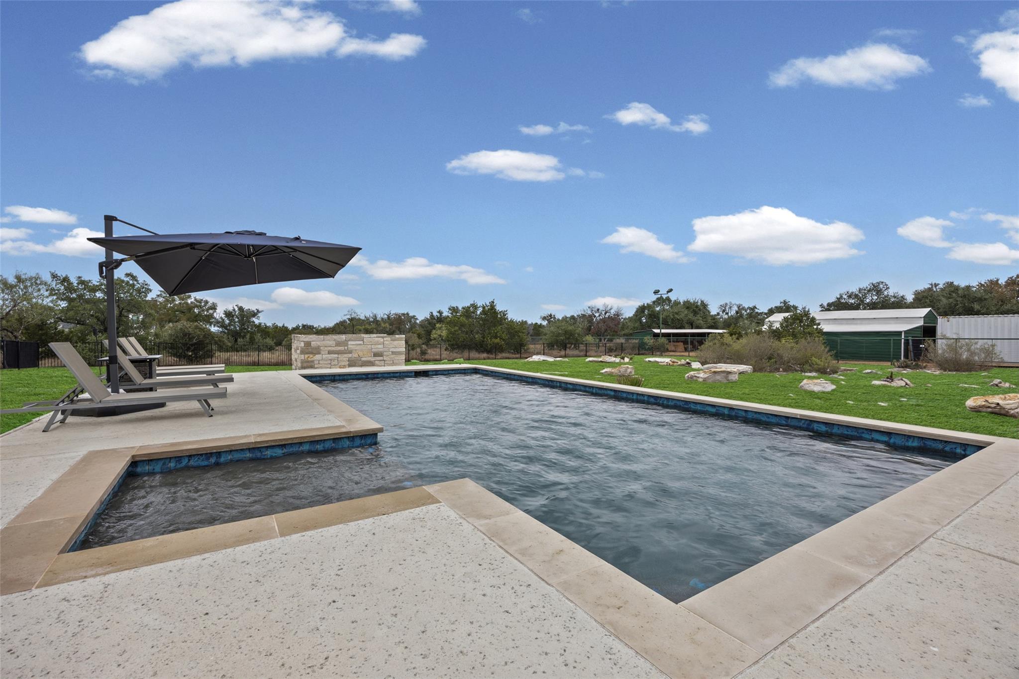 Backyard swimming pool with a stone patio, lounge chairs, and a large umbrella.