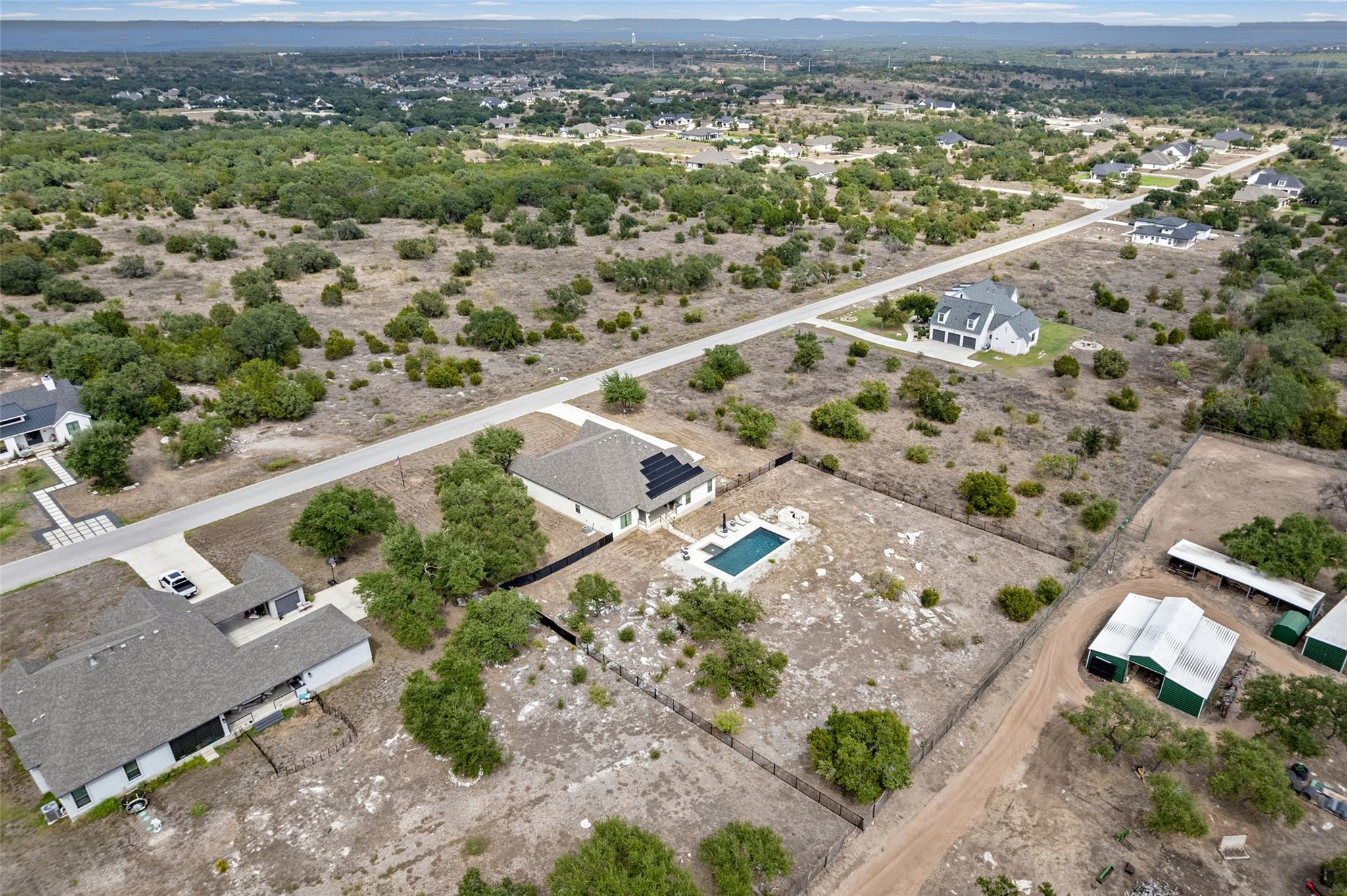 Aerial view of a home with a rectangular pool, fenced yard, and open scrubland nearby.