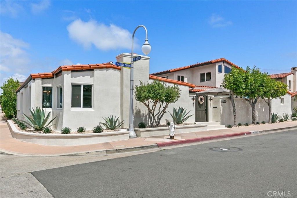 Stucco corner property with red tile roofs, a dark entry gate, and drought-tolerant landscaping.