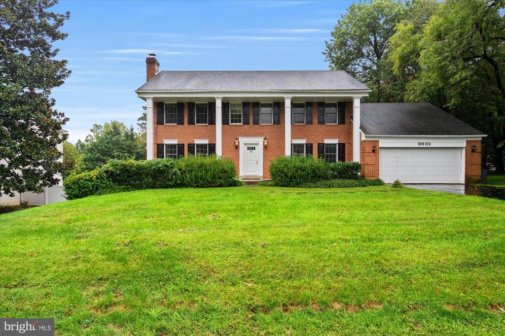Two-story brick house with white columns, an attached garage, and a broad green lawn.