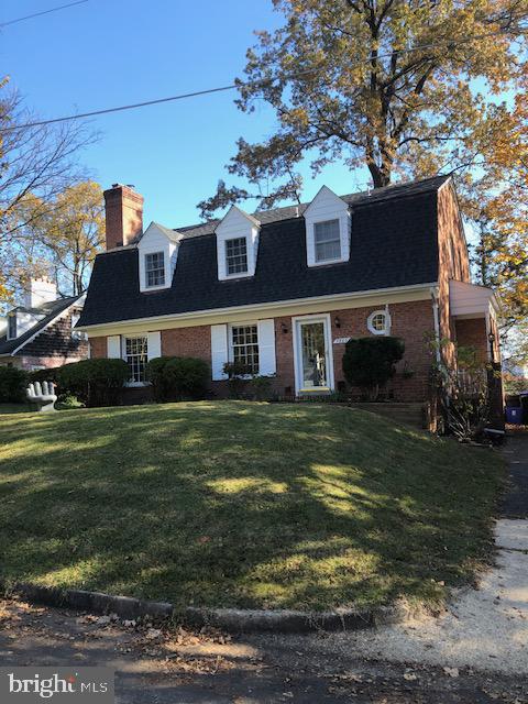 Brick house with three roof dormers, trimmed shrubs, and a sloped front lawn.