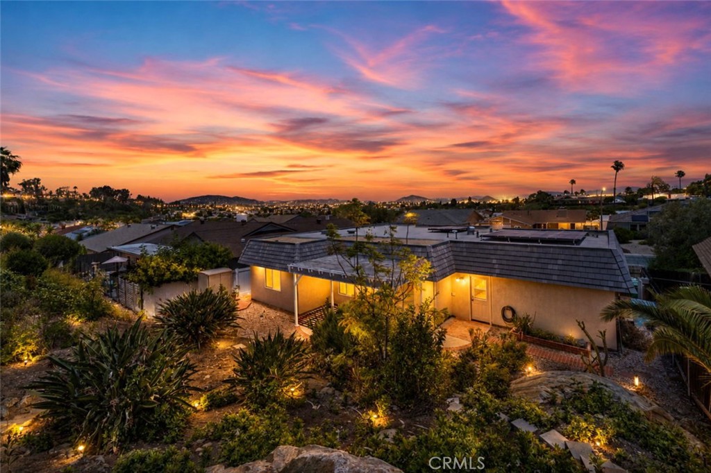 Rear exterior of a single-story home and landscaped yard beneath a vivid sunset.