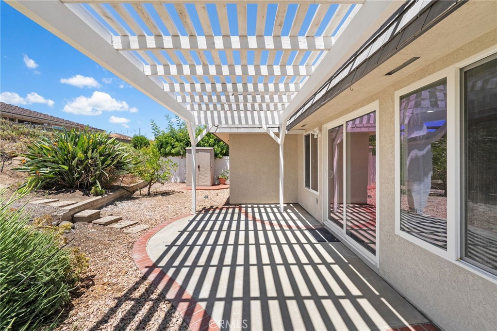 Curved patio under a white slatted pergola beside sliding glass doors and gravel landscaping.