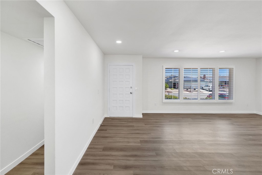 Vacant living room with wood-look flooring, a paneled entry door, and shuttered street-facing windows.