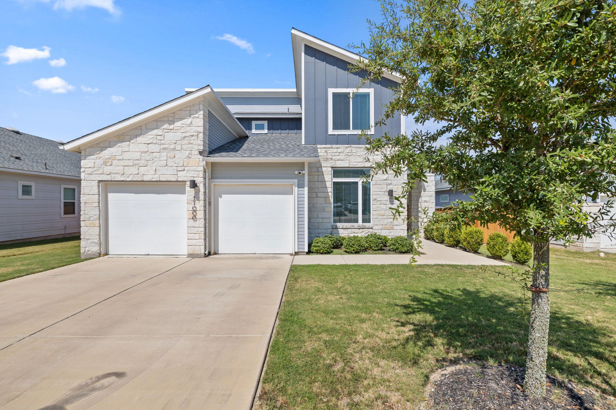 Two-story stone and blue-gray home with two garage doors and a wide driveway.