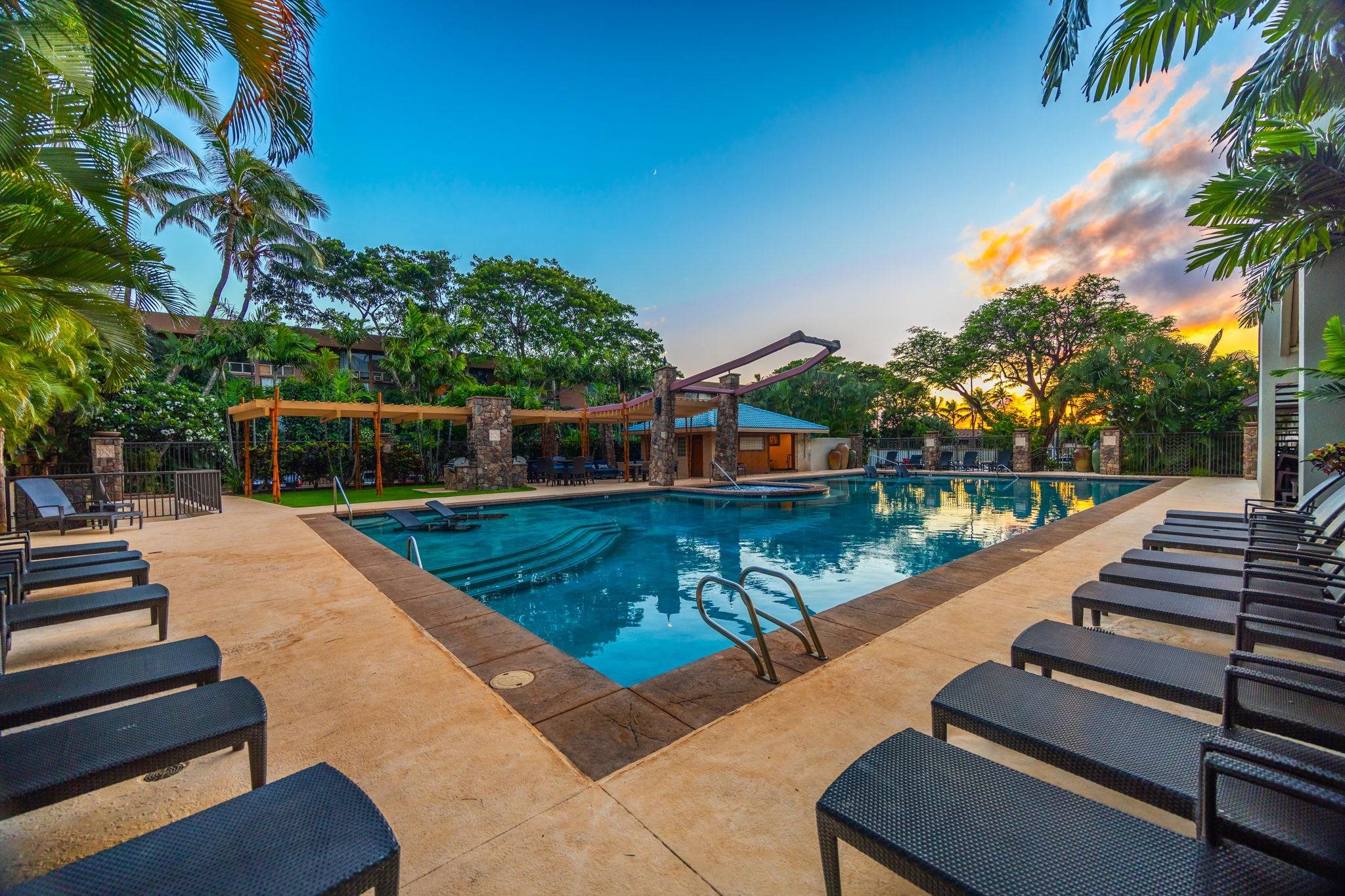 Resort swimming pool with lounge chairs and tropical palms at sunset.