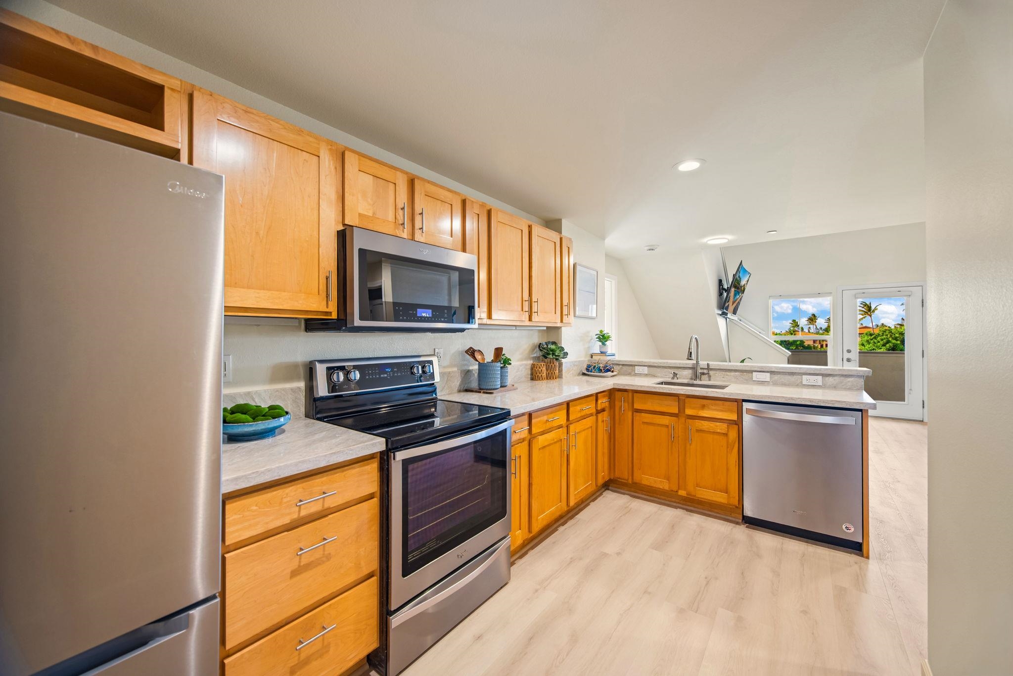 Kitchen with honey-colored cabinets, stainless appliances, and palm trees visible through the glass door.