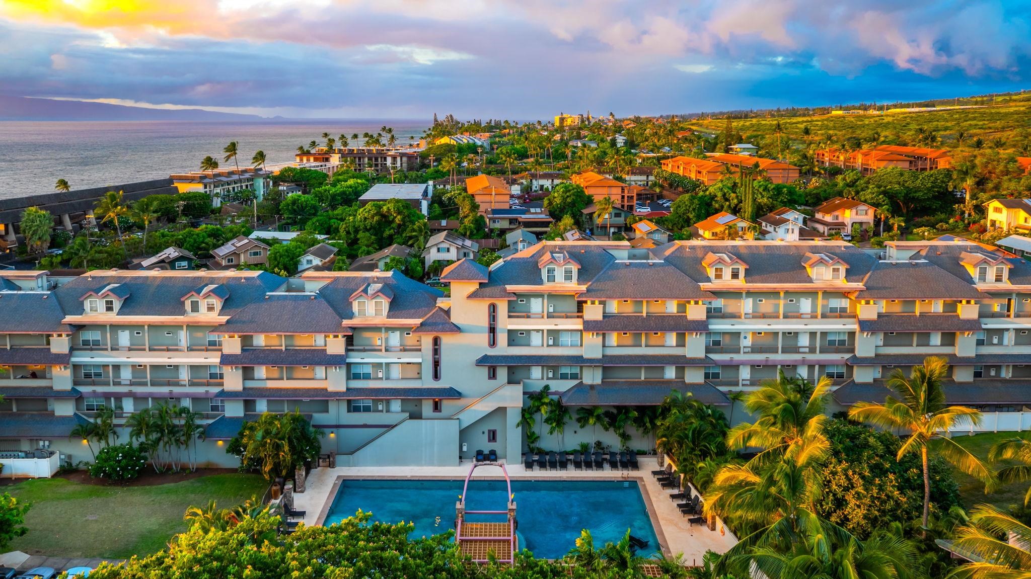 Aerial view of Lahaina condos, pool, palms, and ocean at sunset.