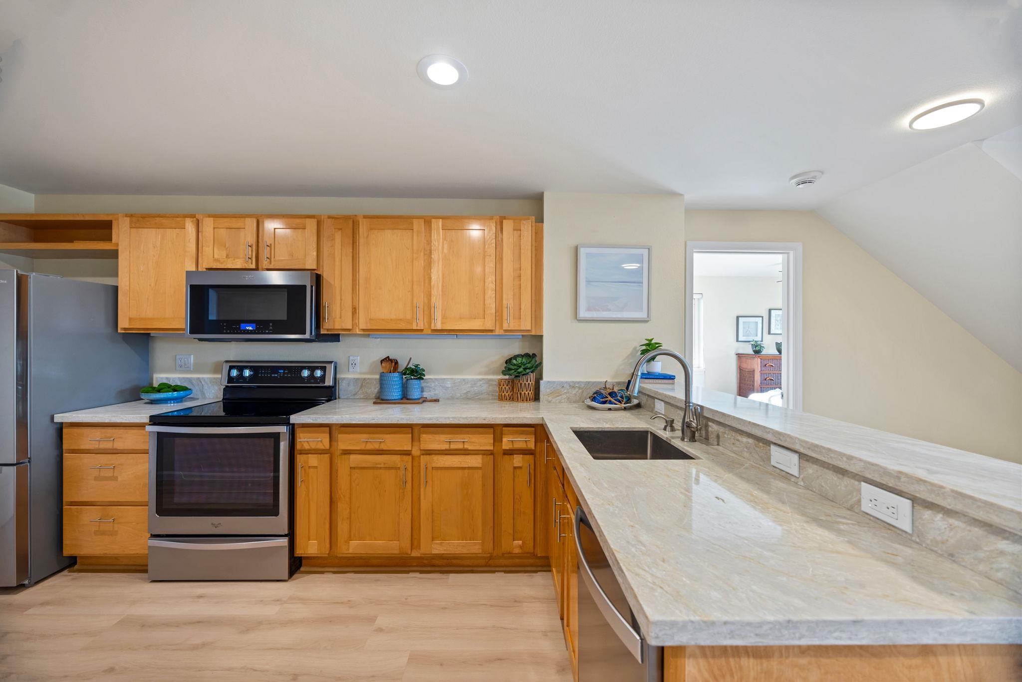 Kitchen with honey-colored cabinets, stainless steel appliances, and a long pale stone peninsula.