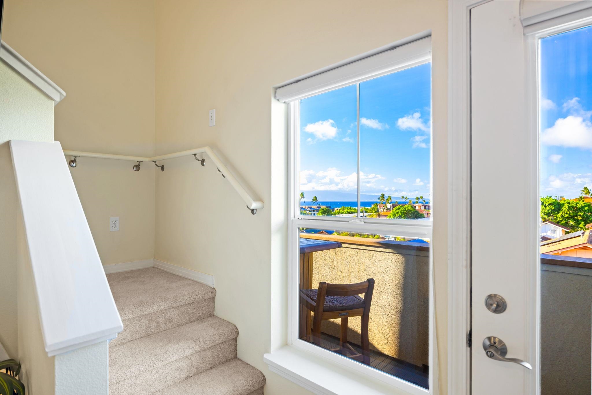 Carpeted staircase beside a window overlooking the ocean, with a chair on the balcony.
