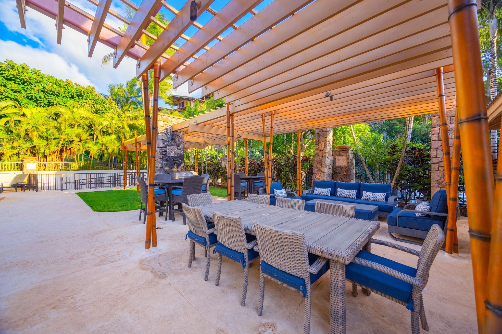 Outdoor patio with pergola, dining table, blue lounge seating, and tropical landscaping.