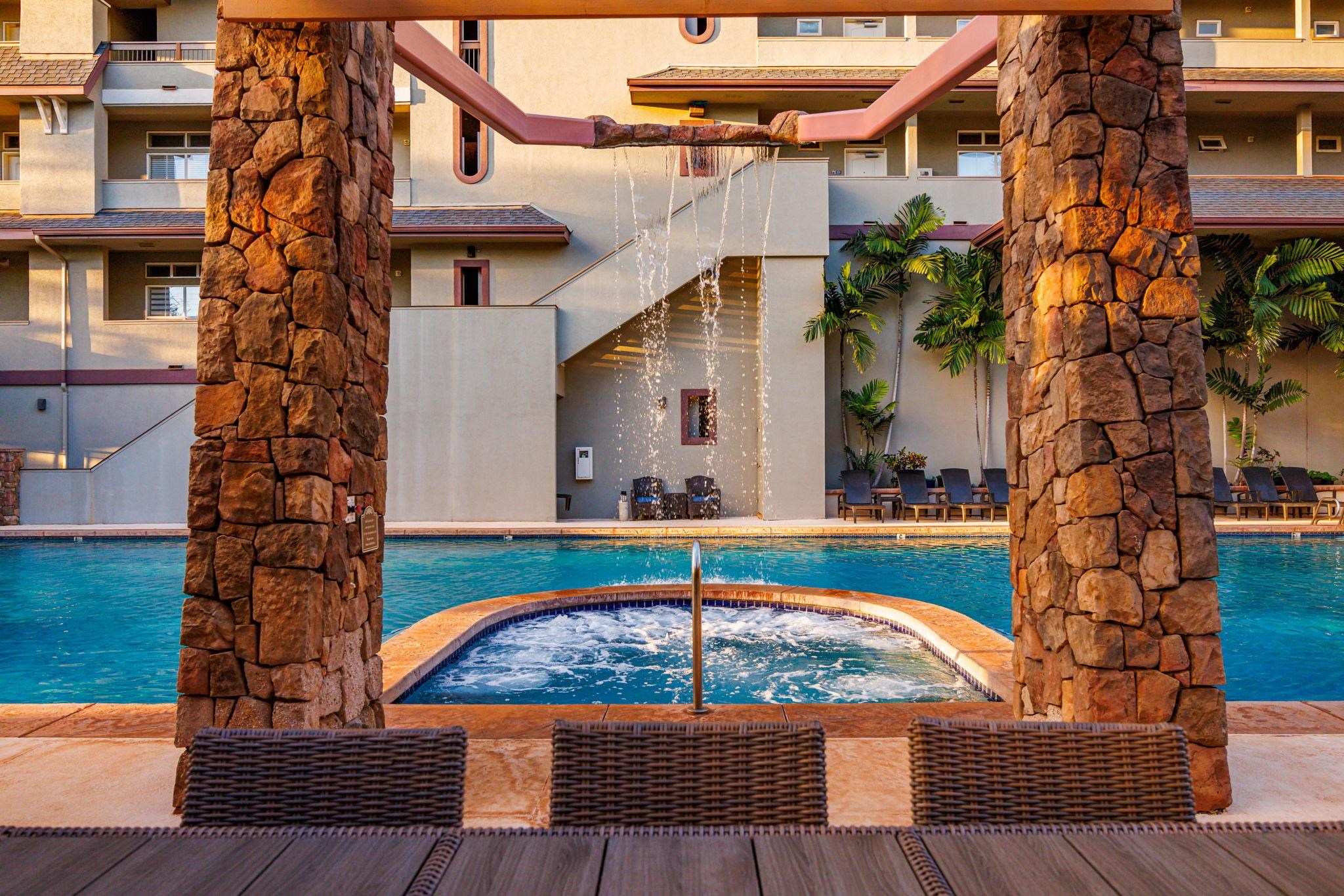 Resort pool and bubbling hot tub framed by stone columns, with a waterfall and tropical palms.