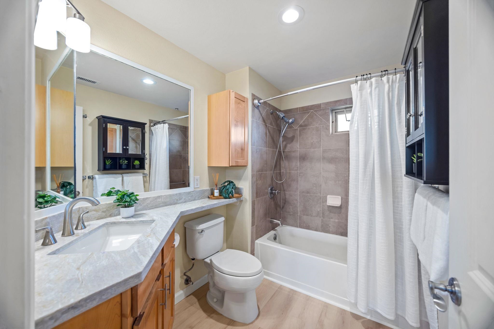 Bathroom with a wood vanity, large mirror, and gray tiled tub-shower surround.