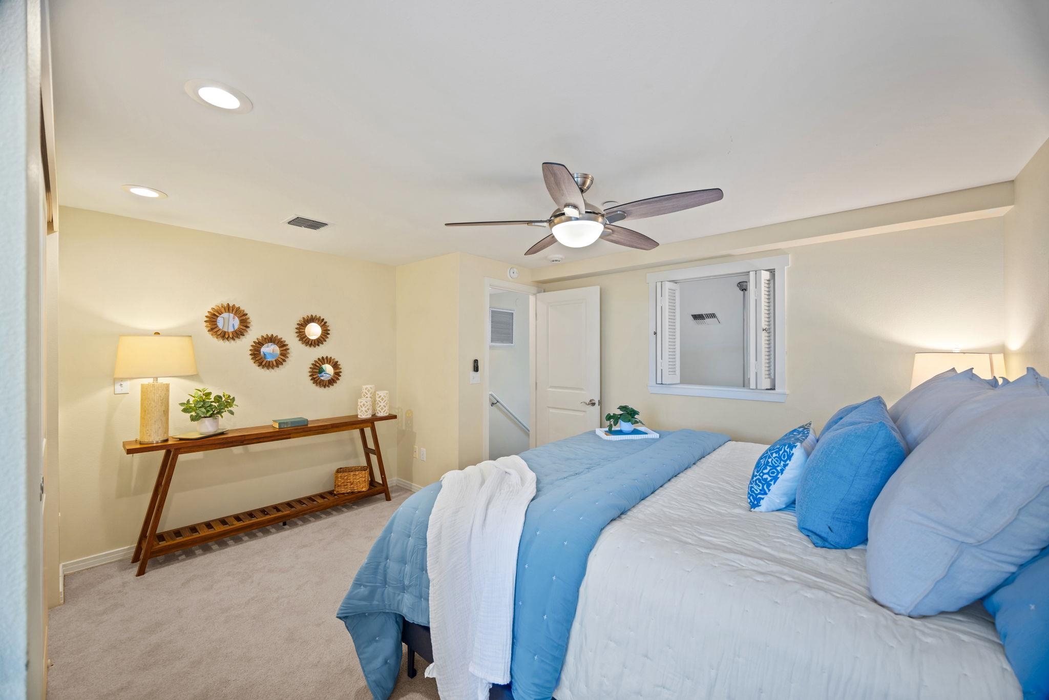 Bedroom with a large bed in blue and white bedding, ceiling fan, and wooden console table.