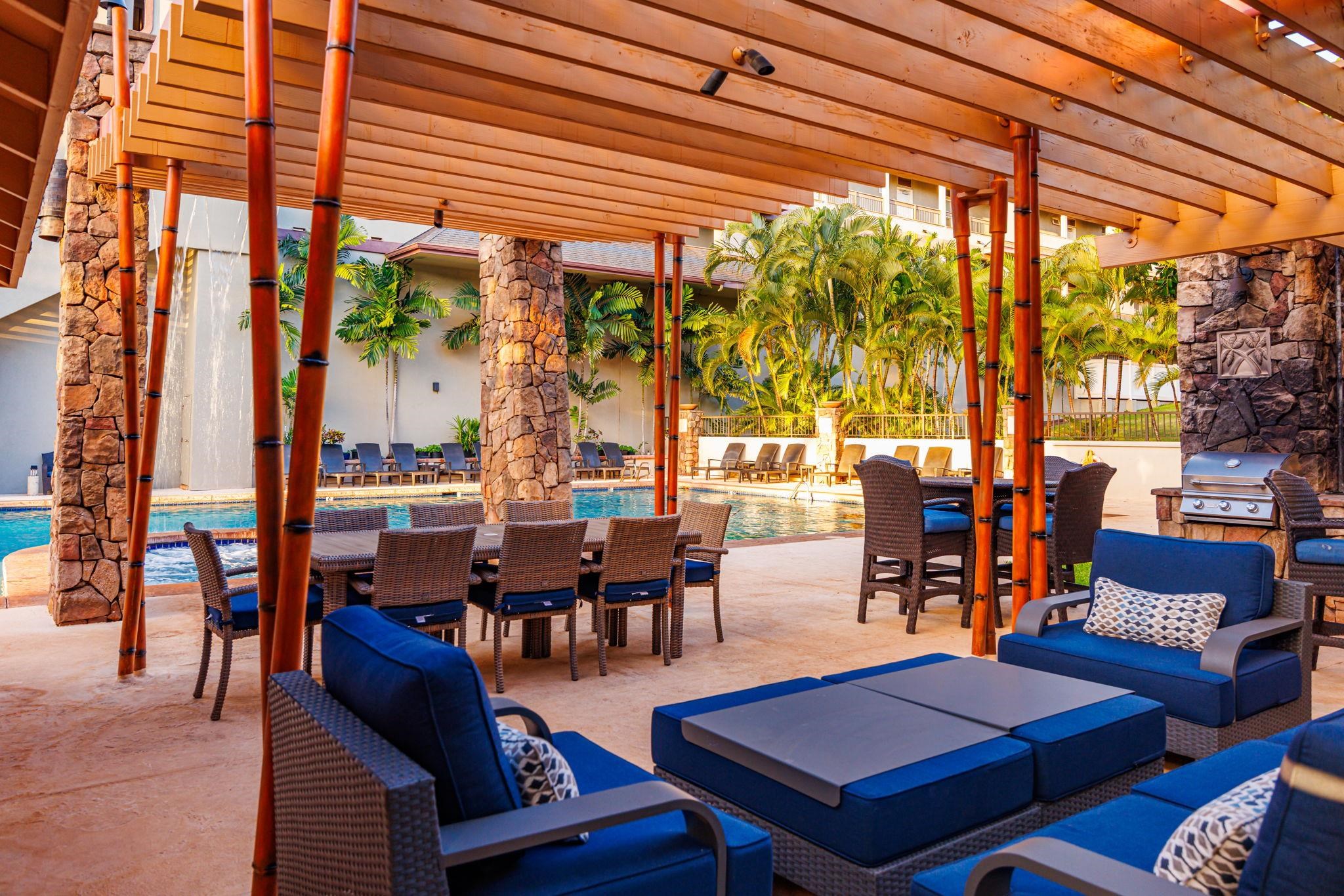 Resort pool beside a pergola-covered patio with blue-cushioned seating and tropical palms.