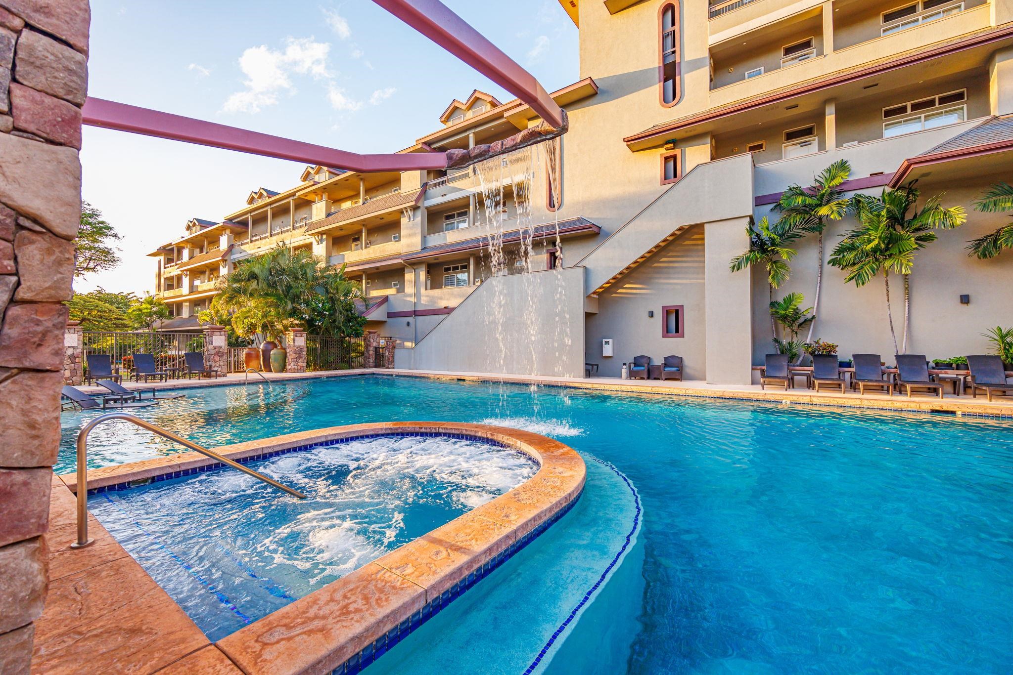 Condominium pool and bubbling circular spa with a cascading waterfall and palm-lined lounge chairs.