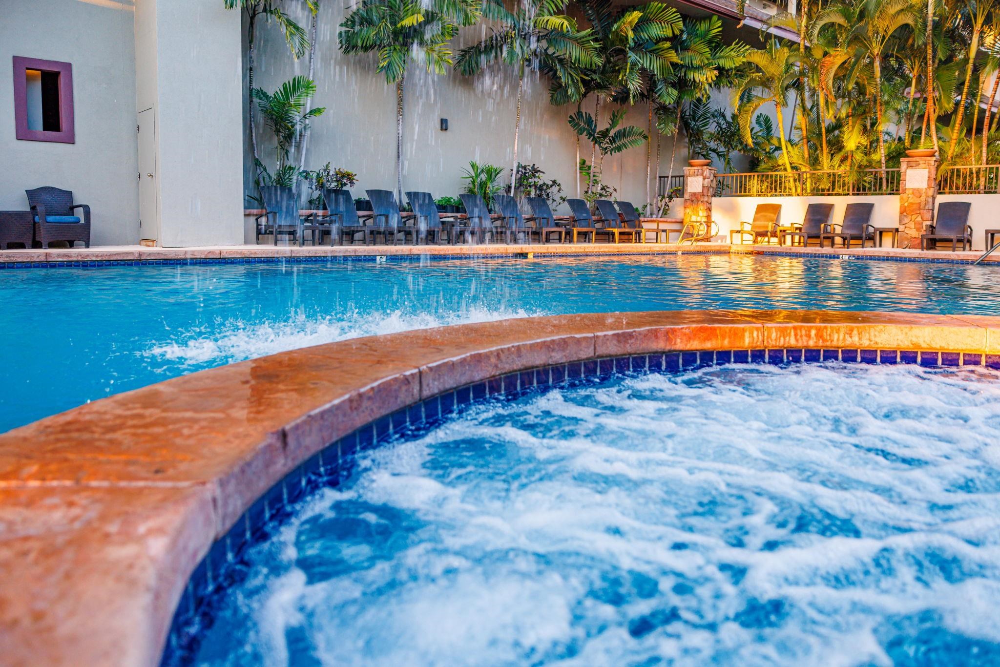Resort pool and bubbling circular spa bordered by lounge chairs and tropical palms.