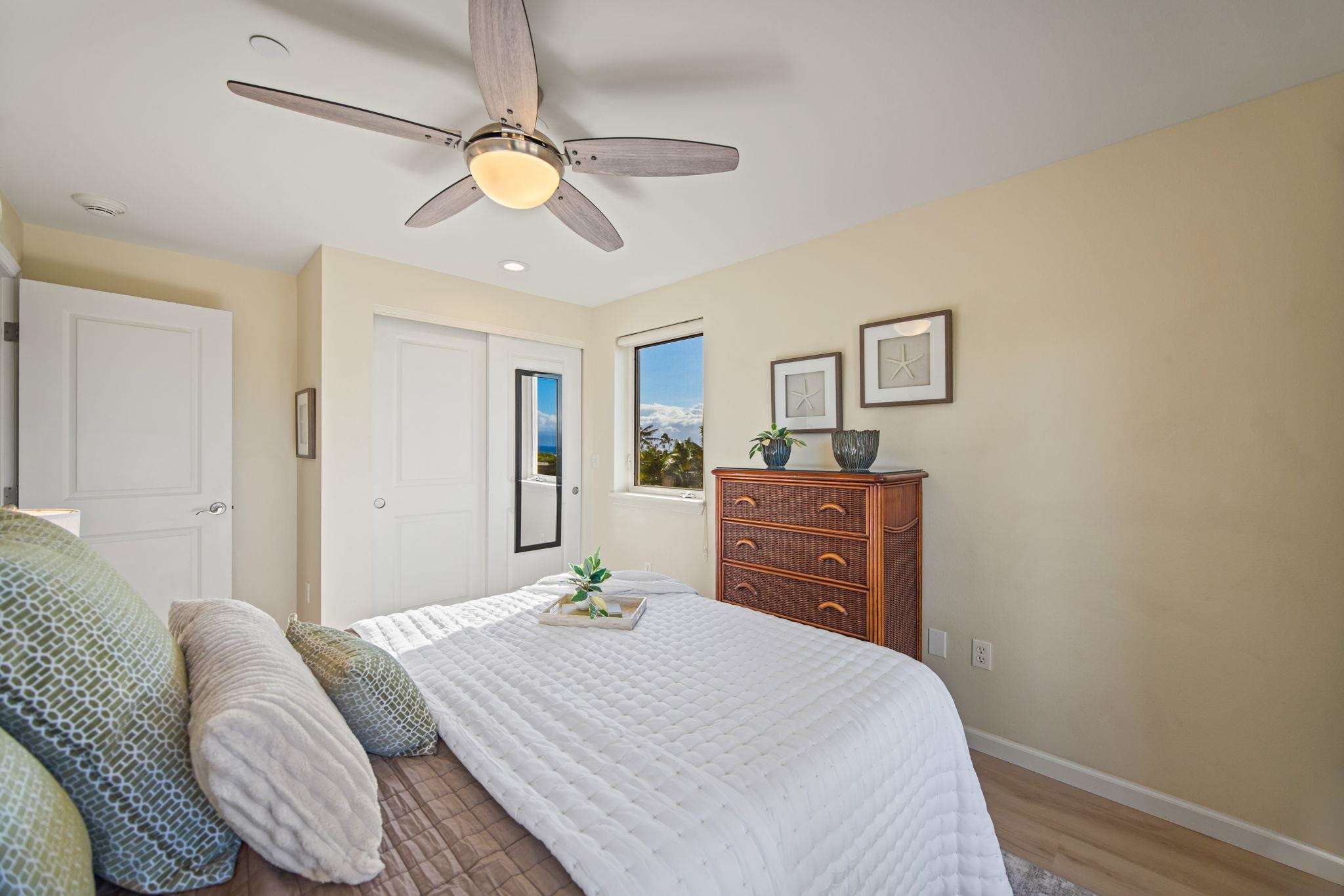 Bedroom with a white quilted bed, wicker-front dresser, and ocean view through the window.