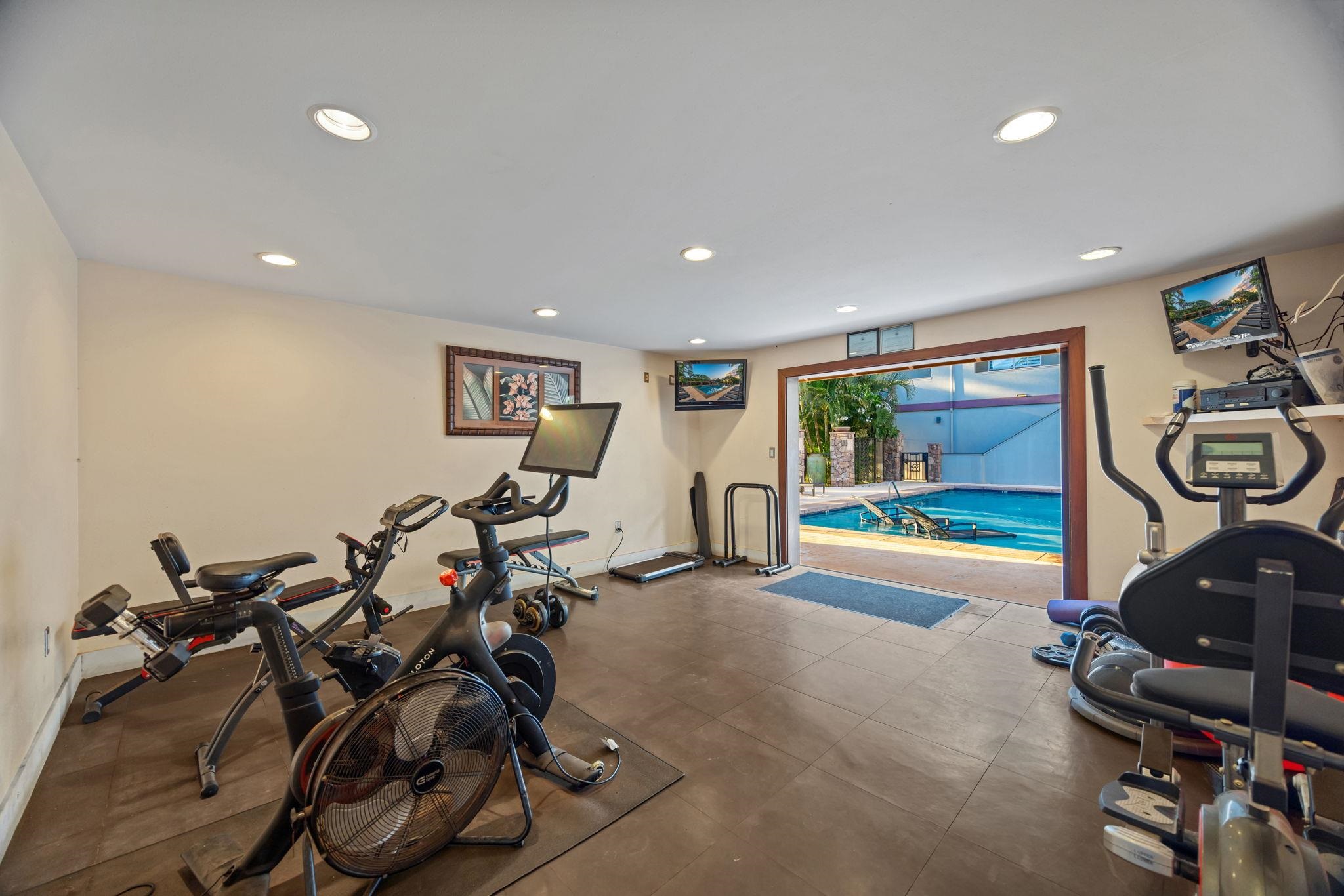 Fitness room with exercise bikes and treadmills opening onto a swimming pool.