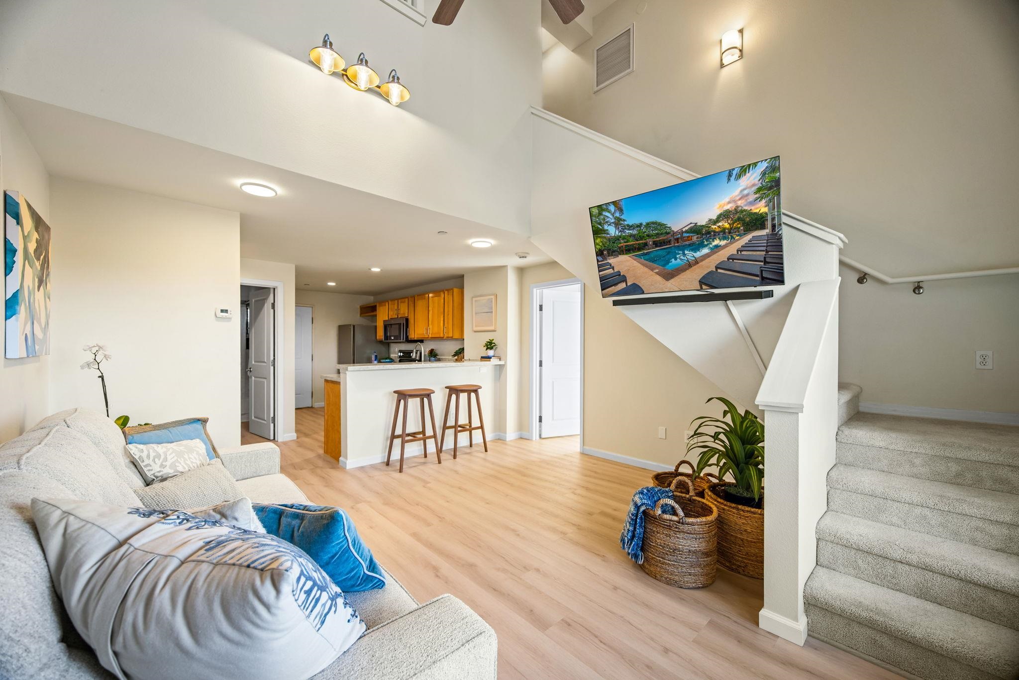 Furnished living room with an open kitchen, vaulted ceiling, and carpeted staircase.