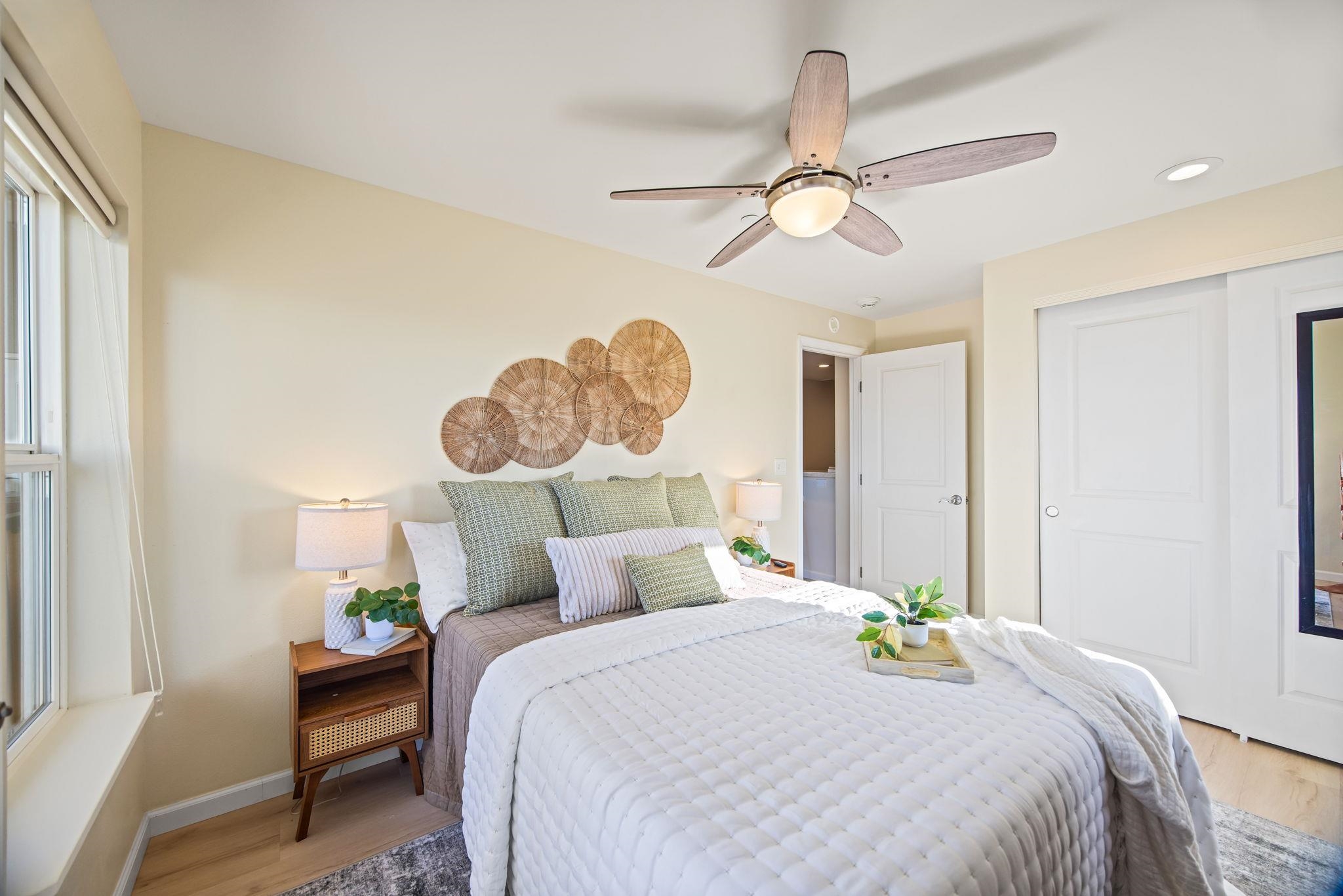 Furnished bedroom with a large white bed, woven wall decor, and a ceiling fan.