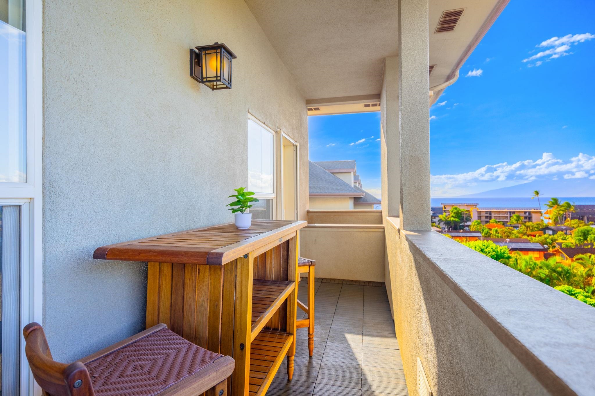 Furnished balcony with wooden table and chairs overlooking the ocean and a distant island.