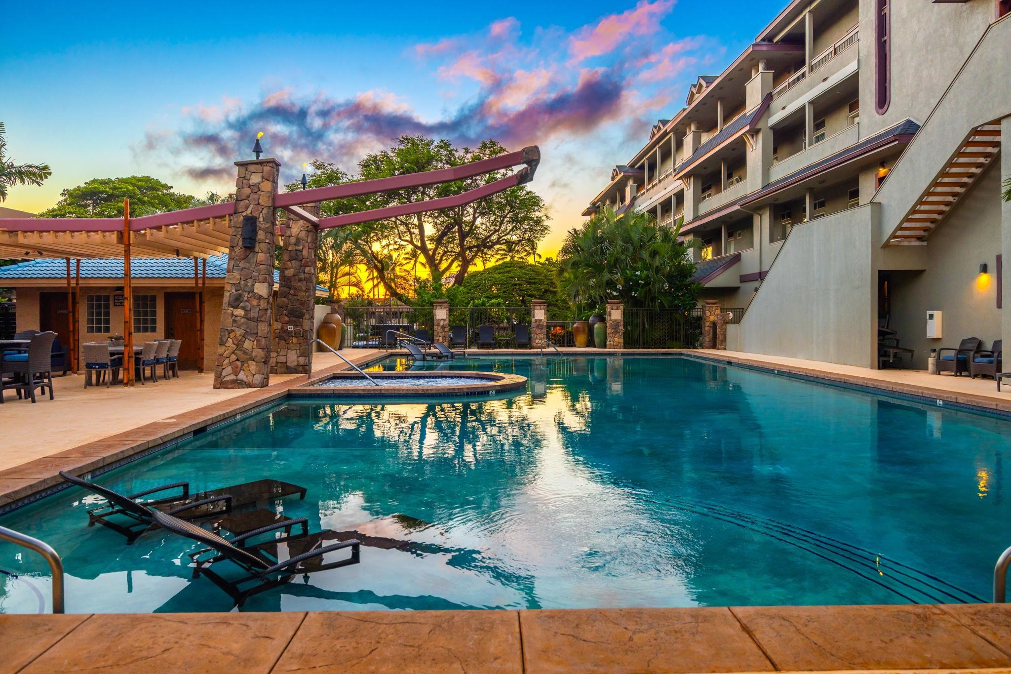 Resort pool and raised spa with in-water loungers beneath a colorful sunset sky.