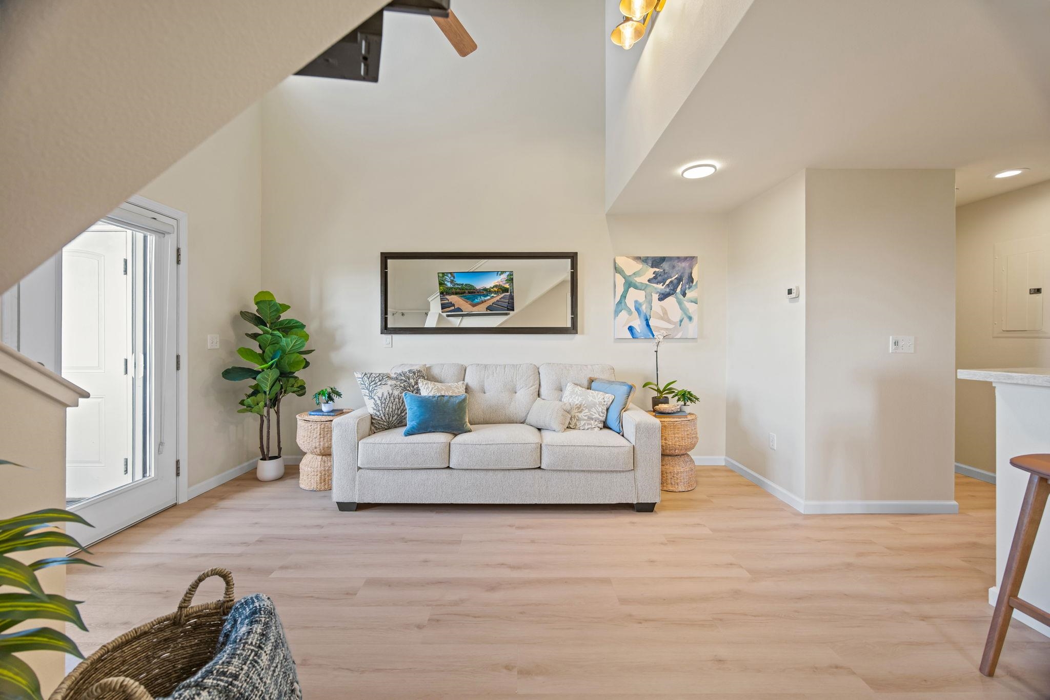 Living room with a gray sofa, blue pillows, pale wood floors, and a staircase in the foreground.