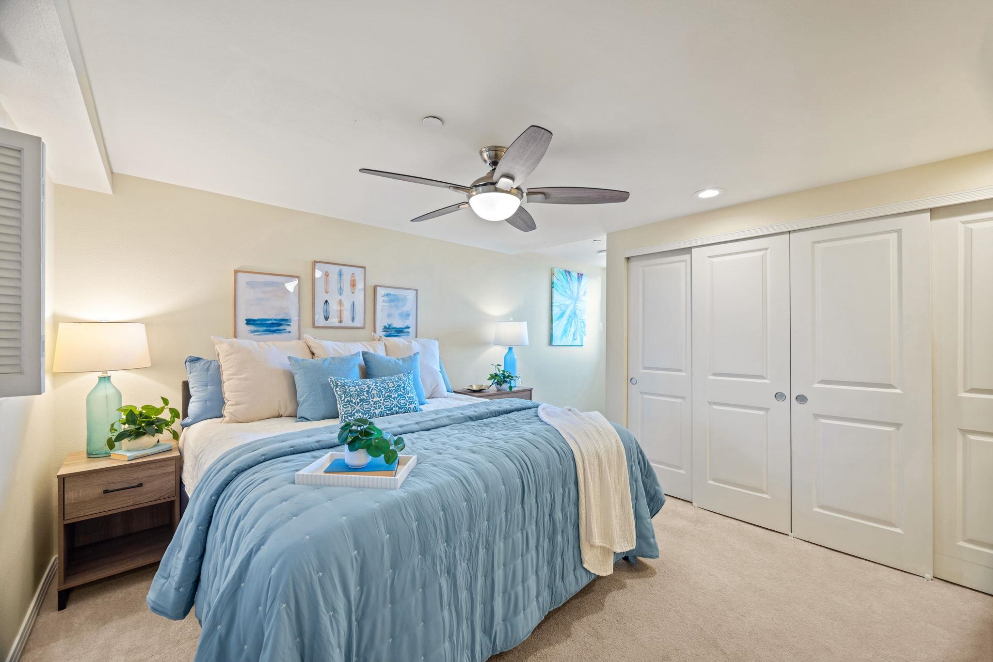 Furnished bedroom with a blue-covered bed, coastal artwork, and white paneled closet doors.