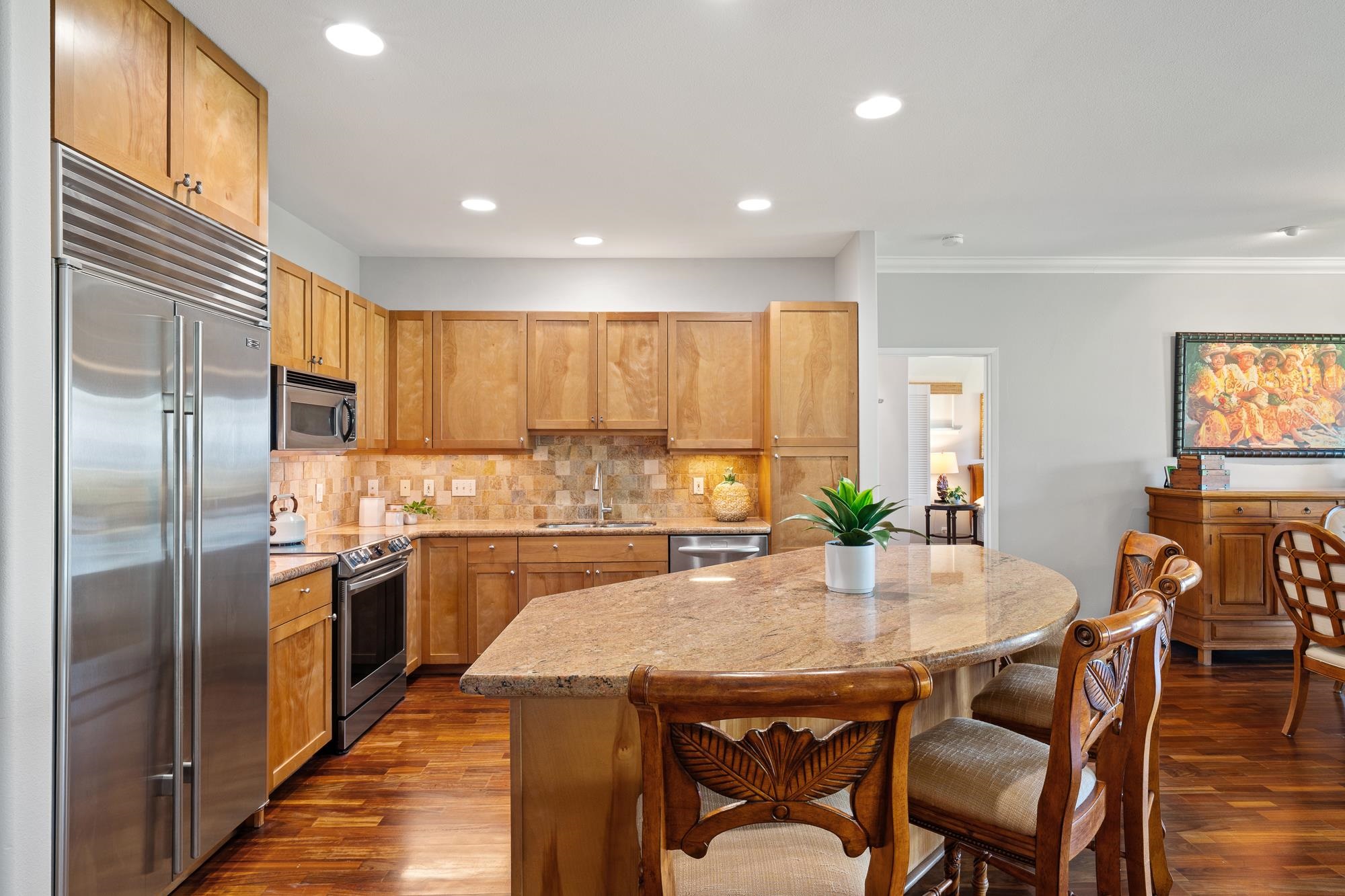 Kitchen with warm wood cabinets, stainless steel appliances, and a large stone island with carved bar stools.